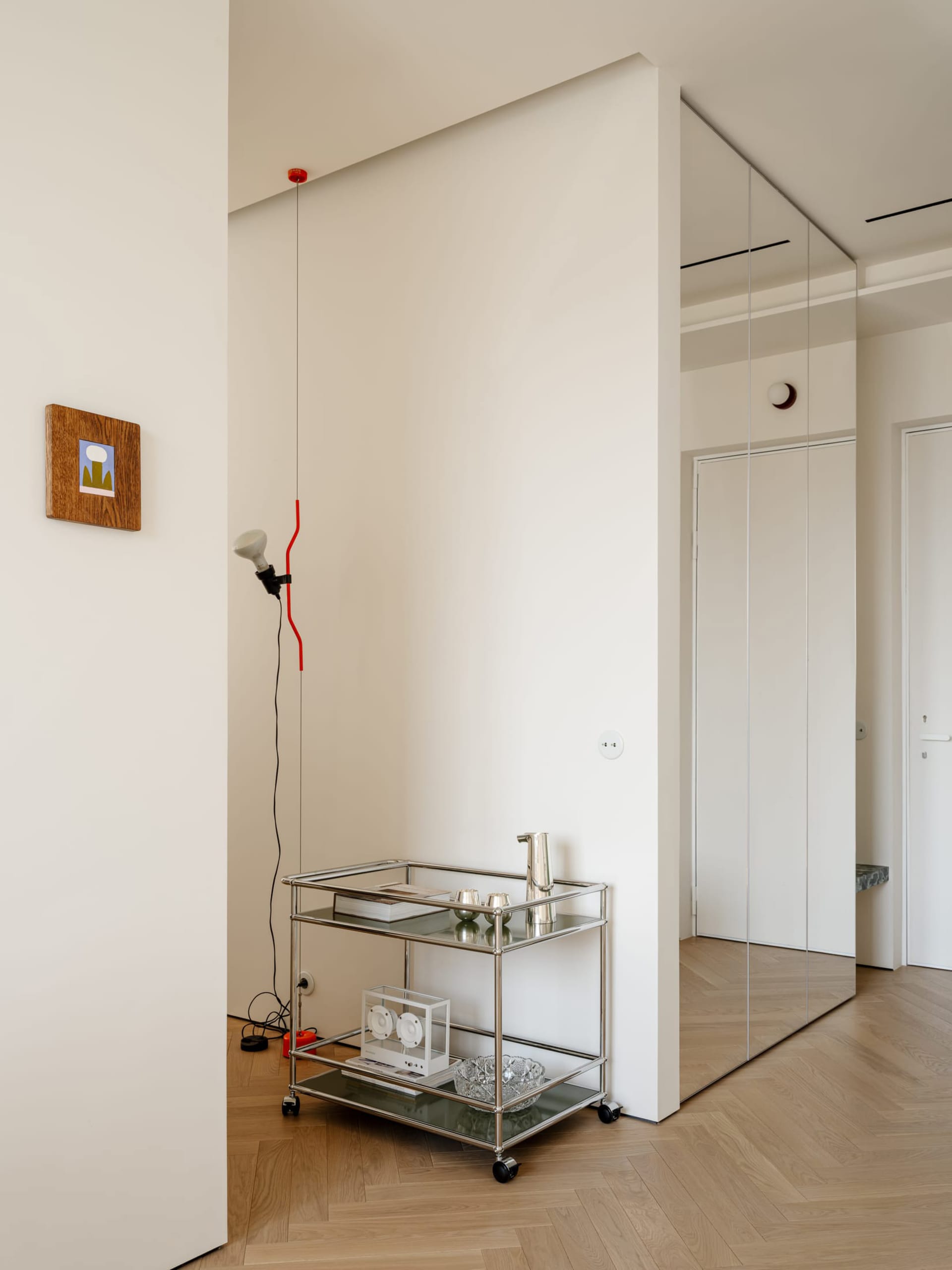 A calm and inviting living space with a white wall, metal shelf, glass clock, and red wire, lit by natural sunlight