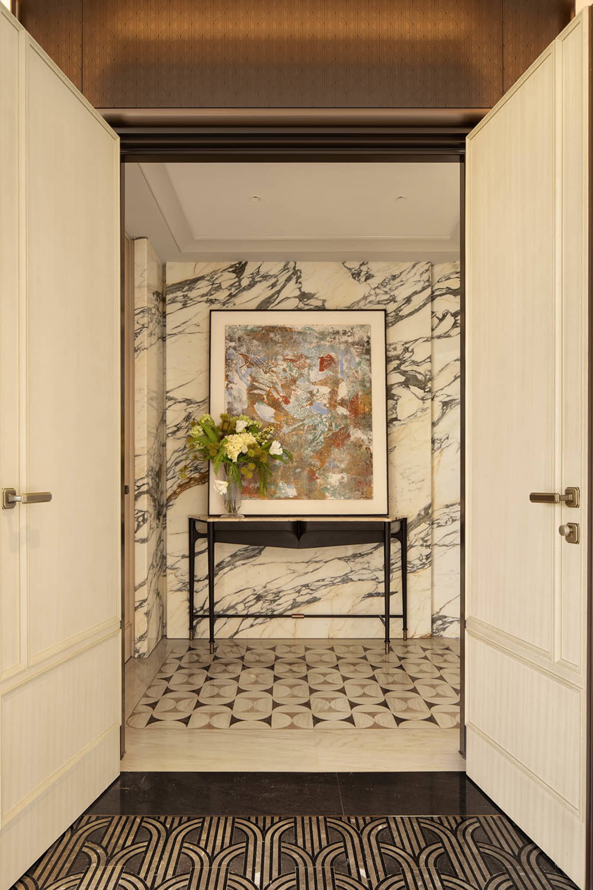 A well-lit hallway with a marble floor, black and white tiles, and a painting on a black frame