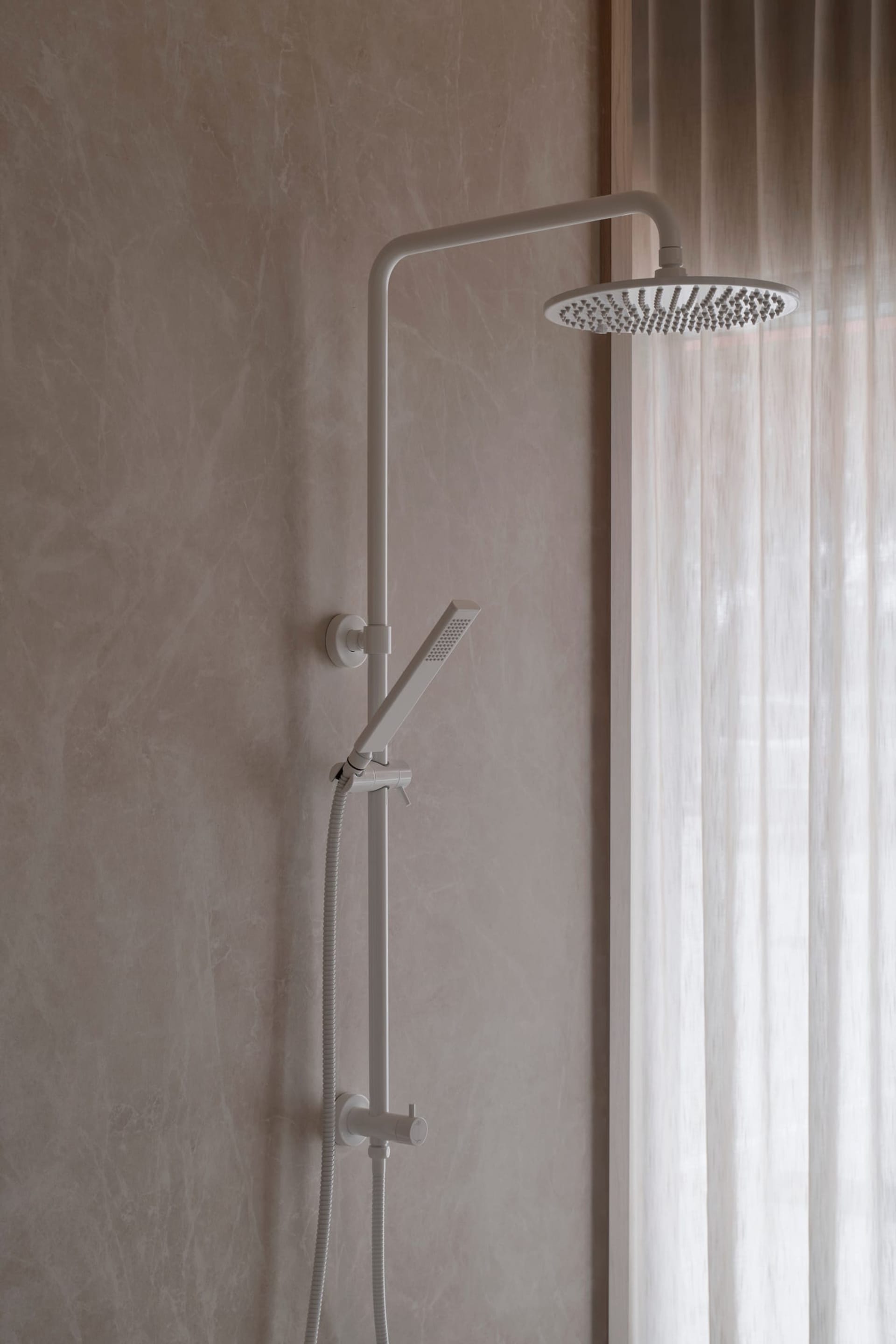 Bathroom with a white shower head on a concrete wall, natural light from a window, and a minimalist aesthetic