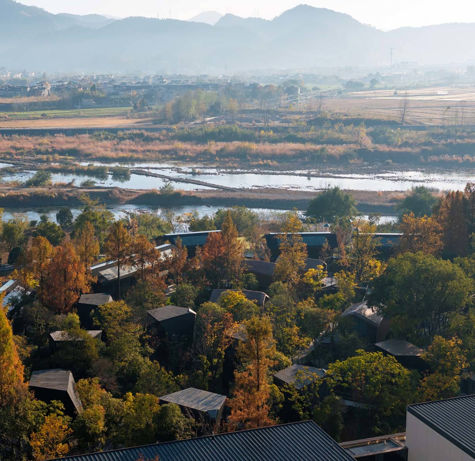 A village with houses and buildings in various architectural styles, surrounded by trees, with natural sunlight and a calm atmosphere