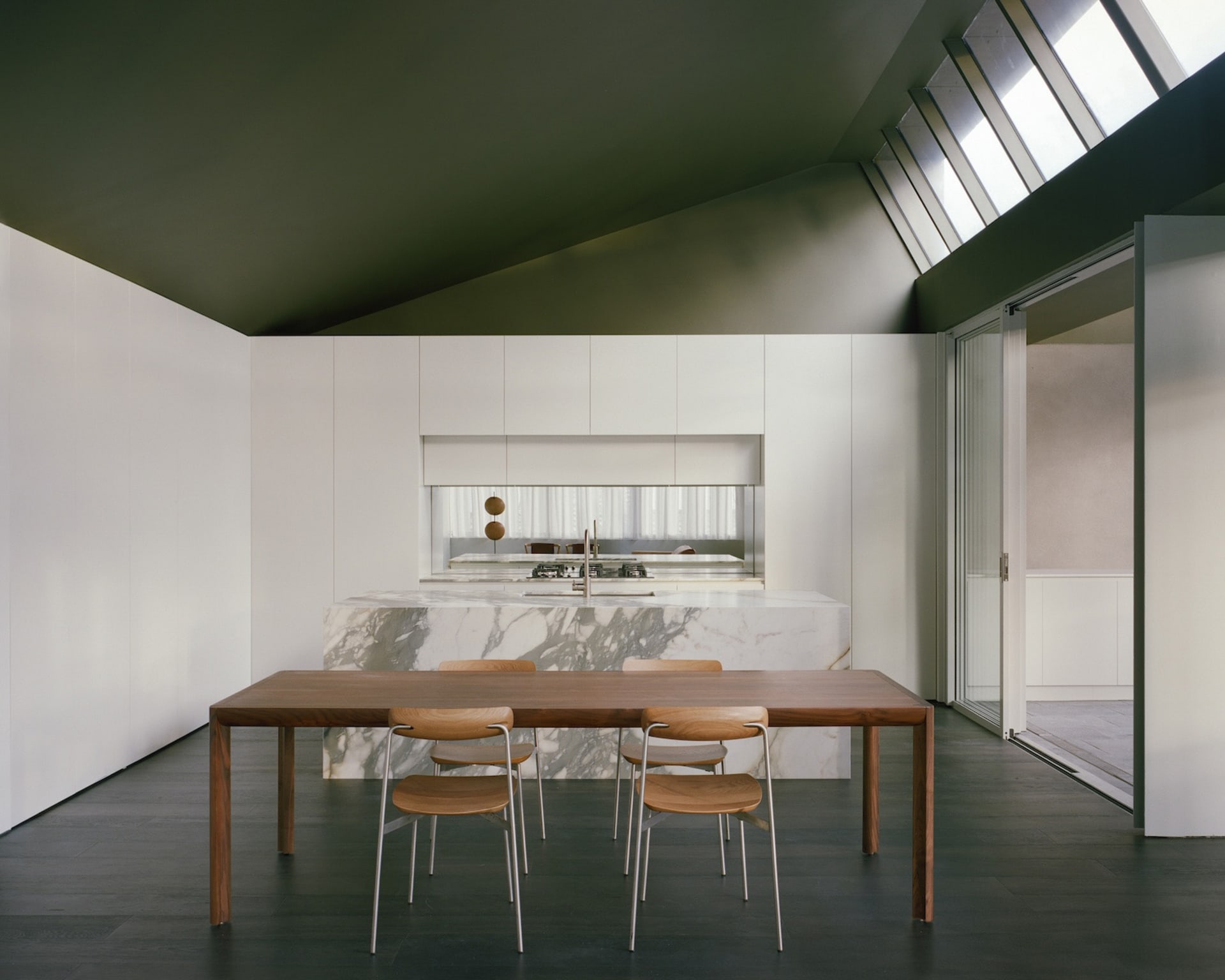 A modern kitchen with a wooden dining table and chairs, surrounded by a sink and oven, in a well-lit space with neutral colors and a focus on wood elements