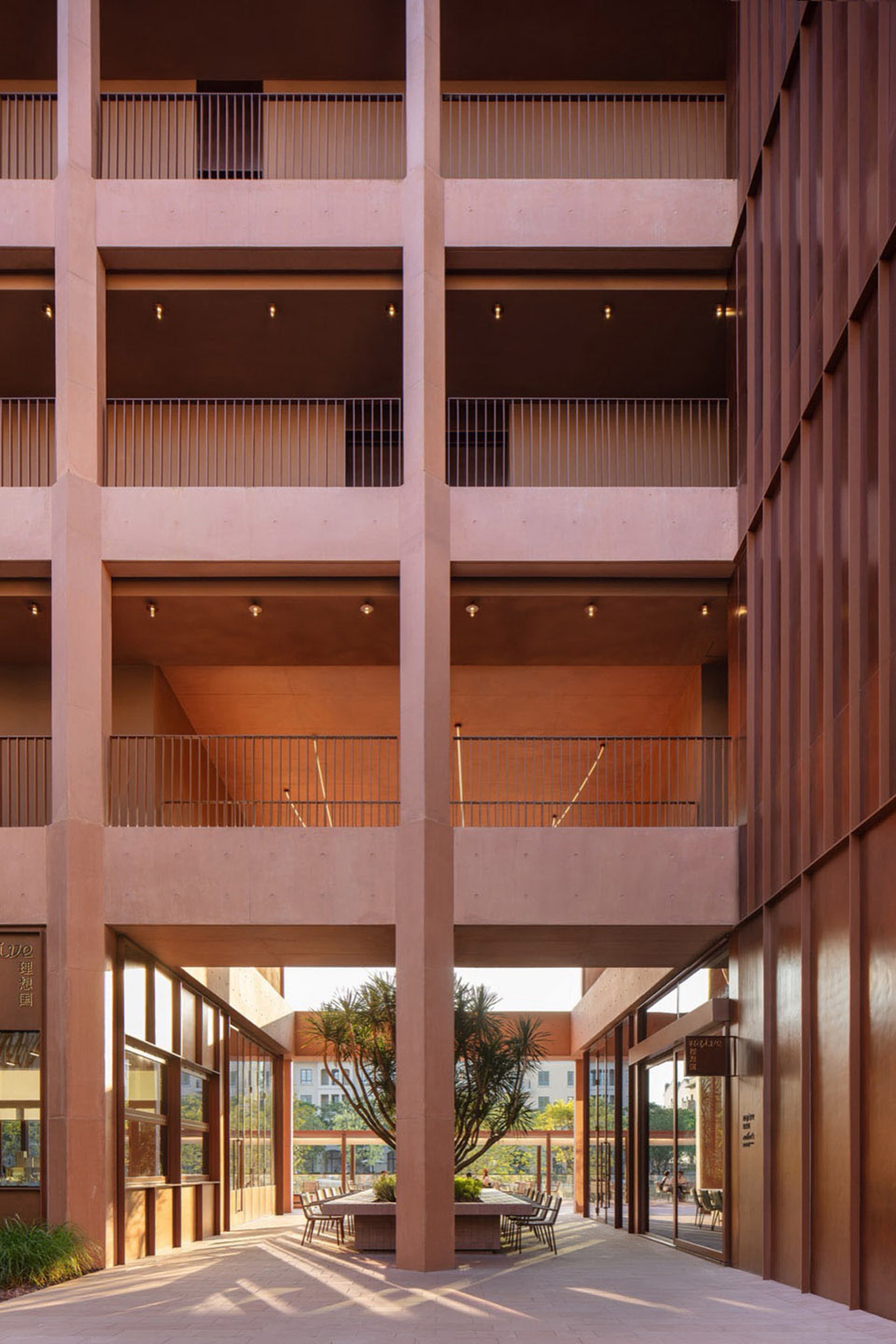 A large, empty building with a red brick exterior, a large atrium, and a balcony on the upper level, bathed in natural light