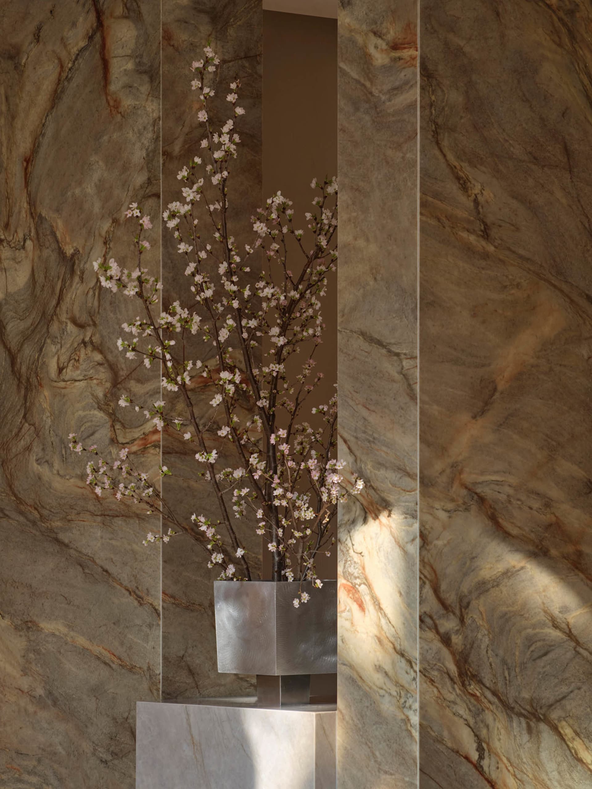 A modern room with a stone wall, a metal vase with white flowers, and soft, diffused lighting