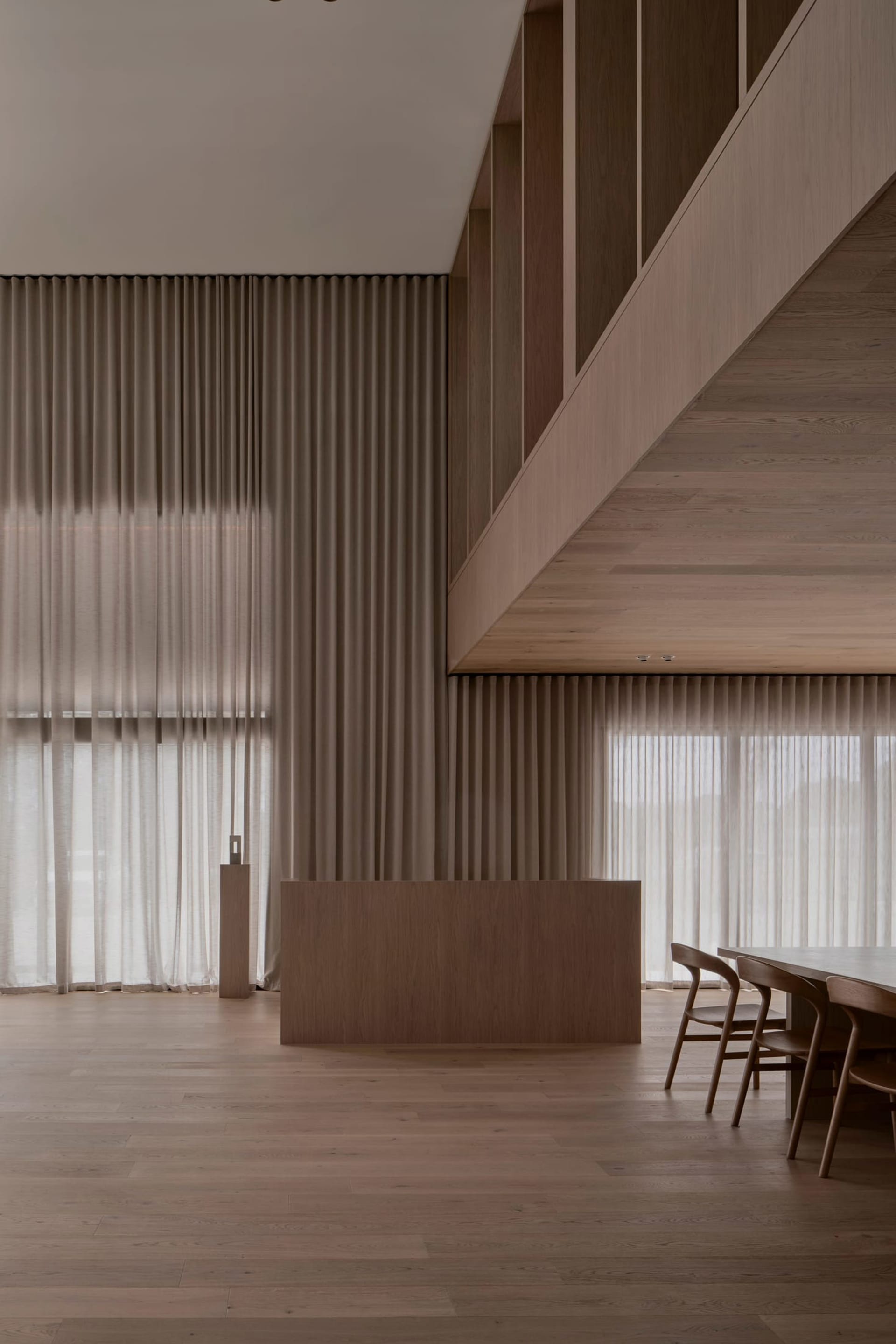 Well-lit living room with wooden floor, walls, and dining table, featuring natural light and a warm atmosphere