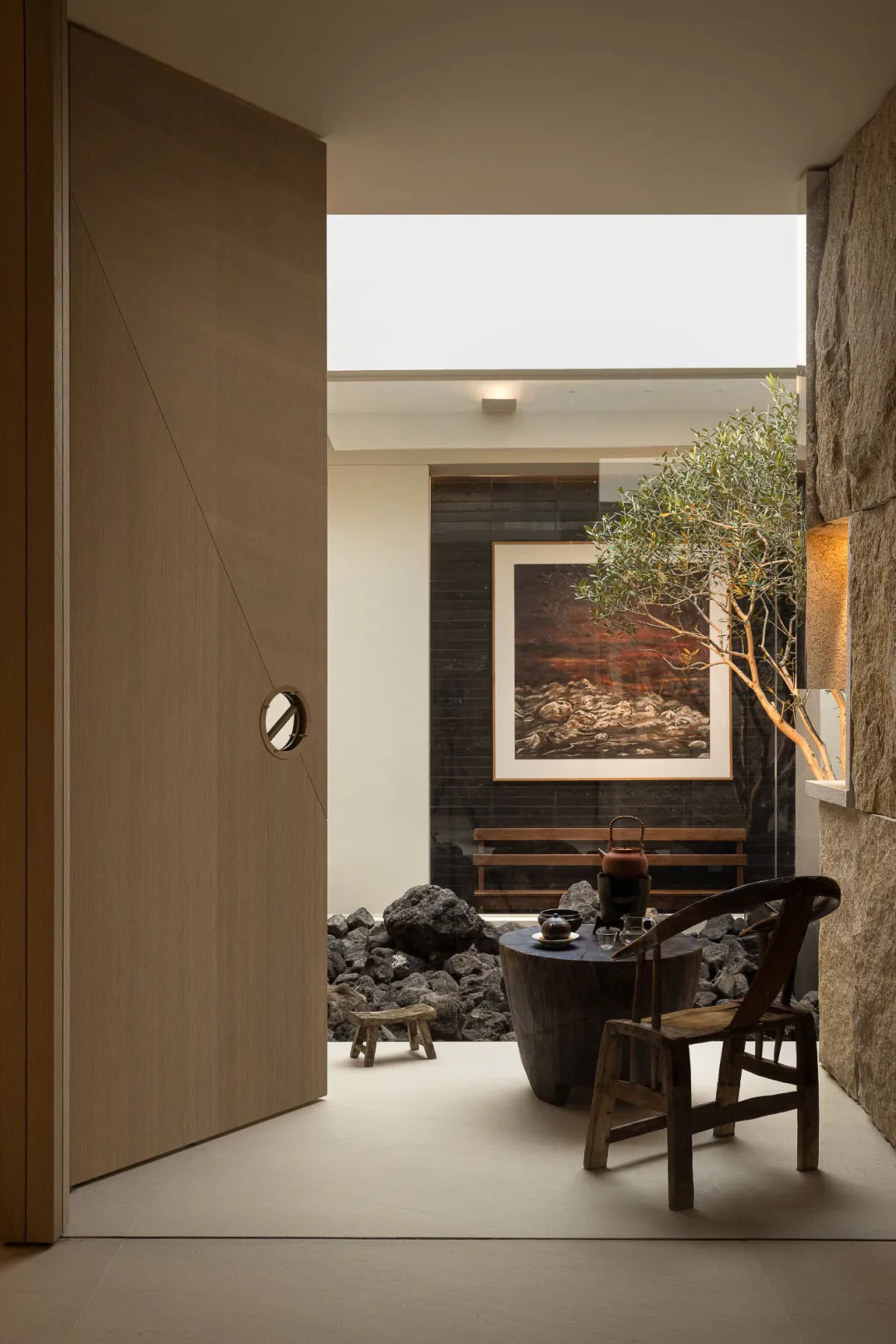 Cozy living space with a wooden door, a bench, a dining table, and a potted plant, set against a stone wall with a wooden floor and dim lighting