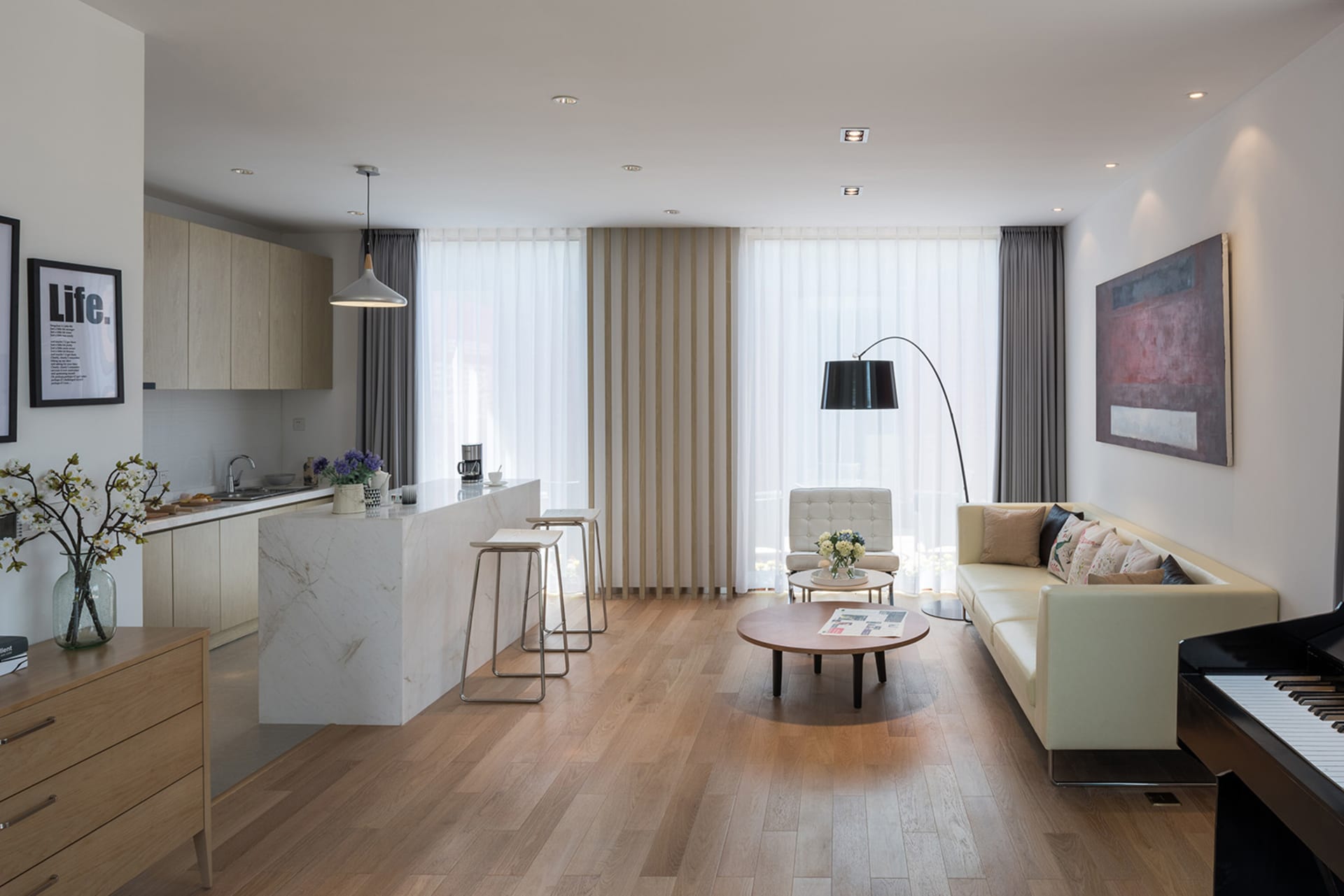 A modern living room with a white couch, chair, and dining table, featuring wood and glass materials, natural light, and a clean design