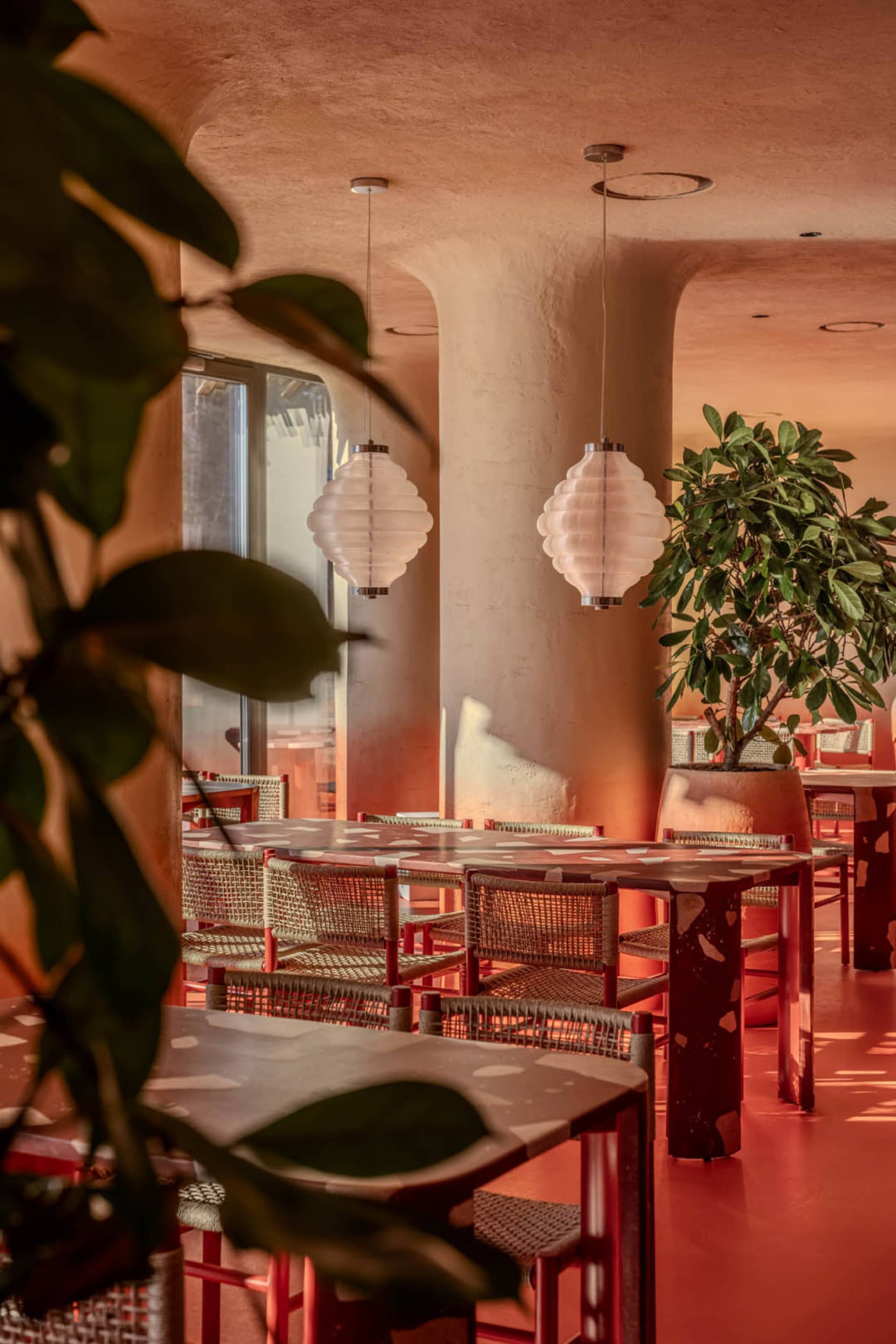 A modern restaurant interior with red and white furniture, potted plants, and warm lighting