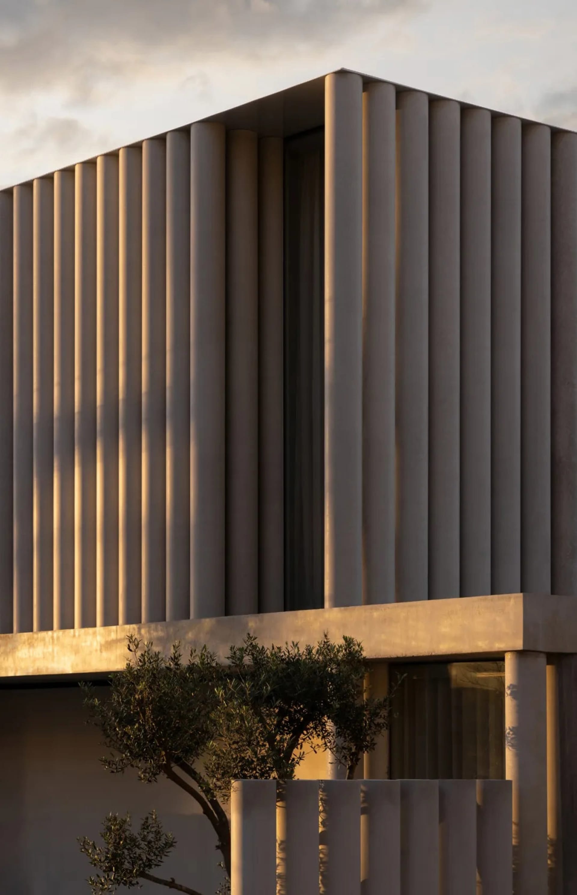 A modern building with a tan exterior, concrete construction, and a large window, set against a warm and inviting natural light background