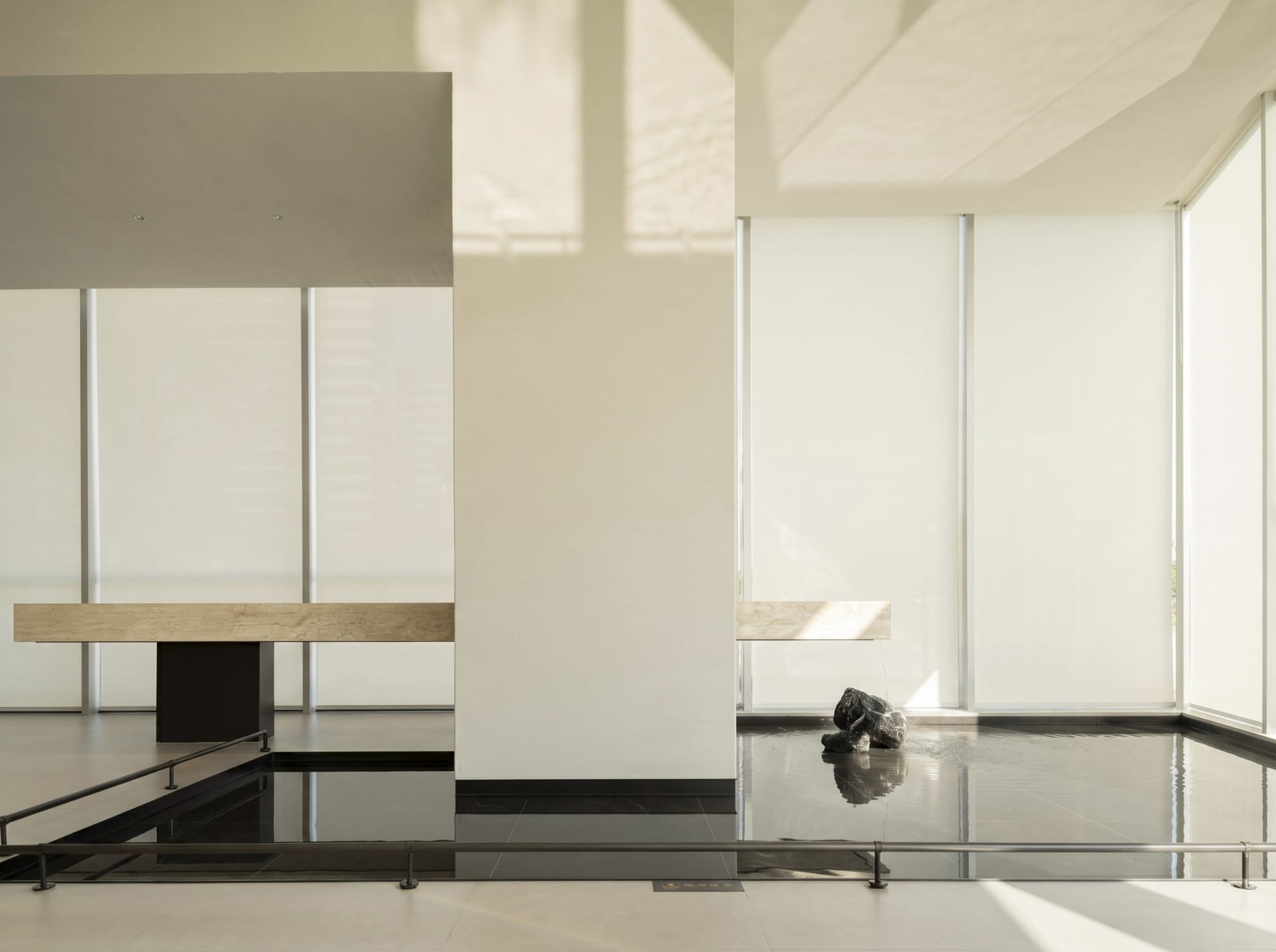 A calm and inviting living room with a black floor, white wall, and natural light from the windows, featuring a modern bench and a dog sitting on it