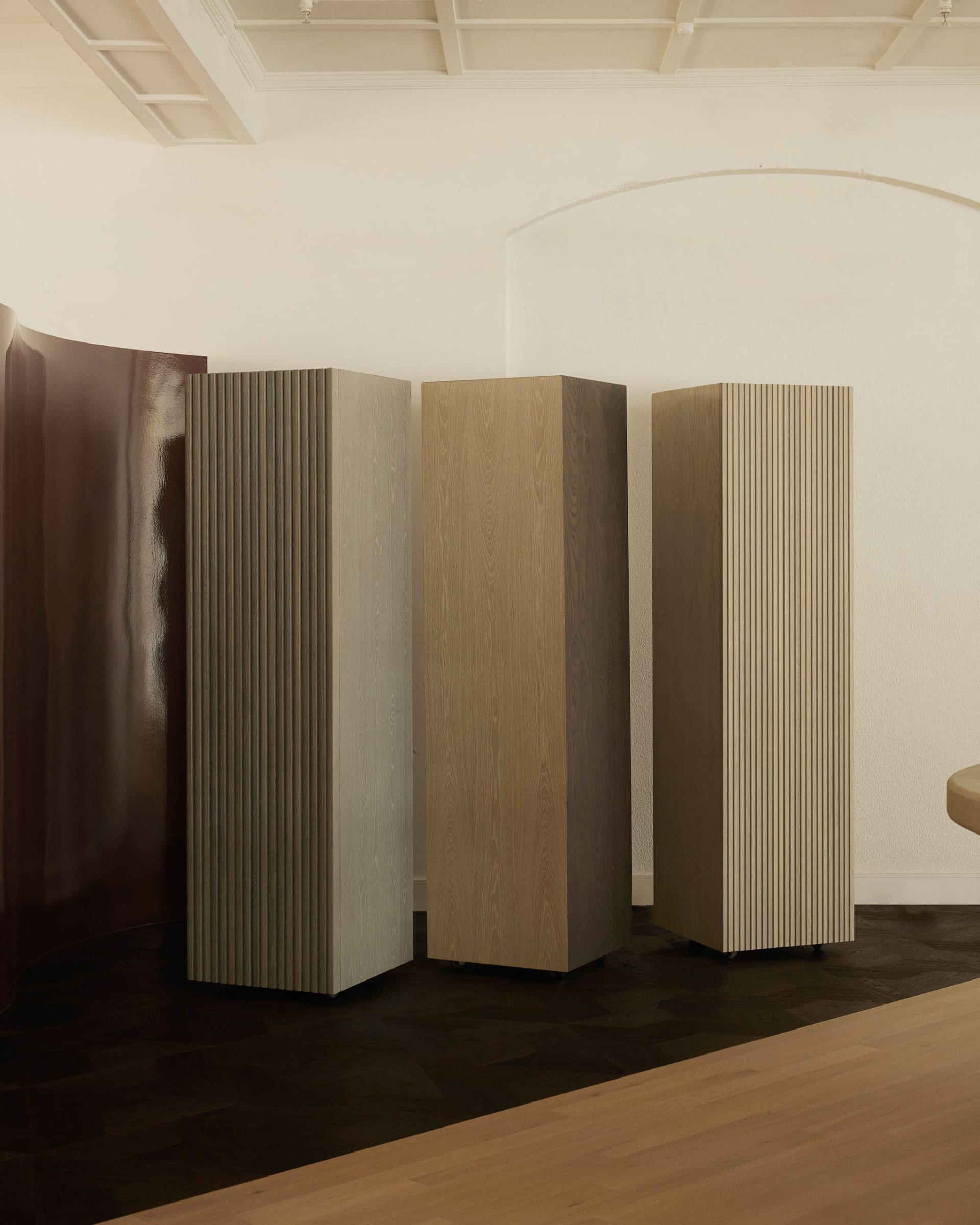A minimalist living space with three tall wooden pillars, a bench in the corner, and a clean design aesthetic