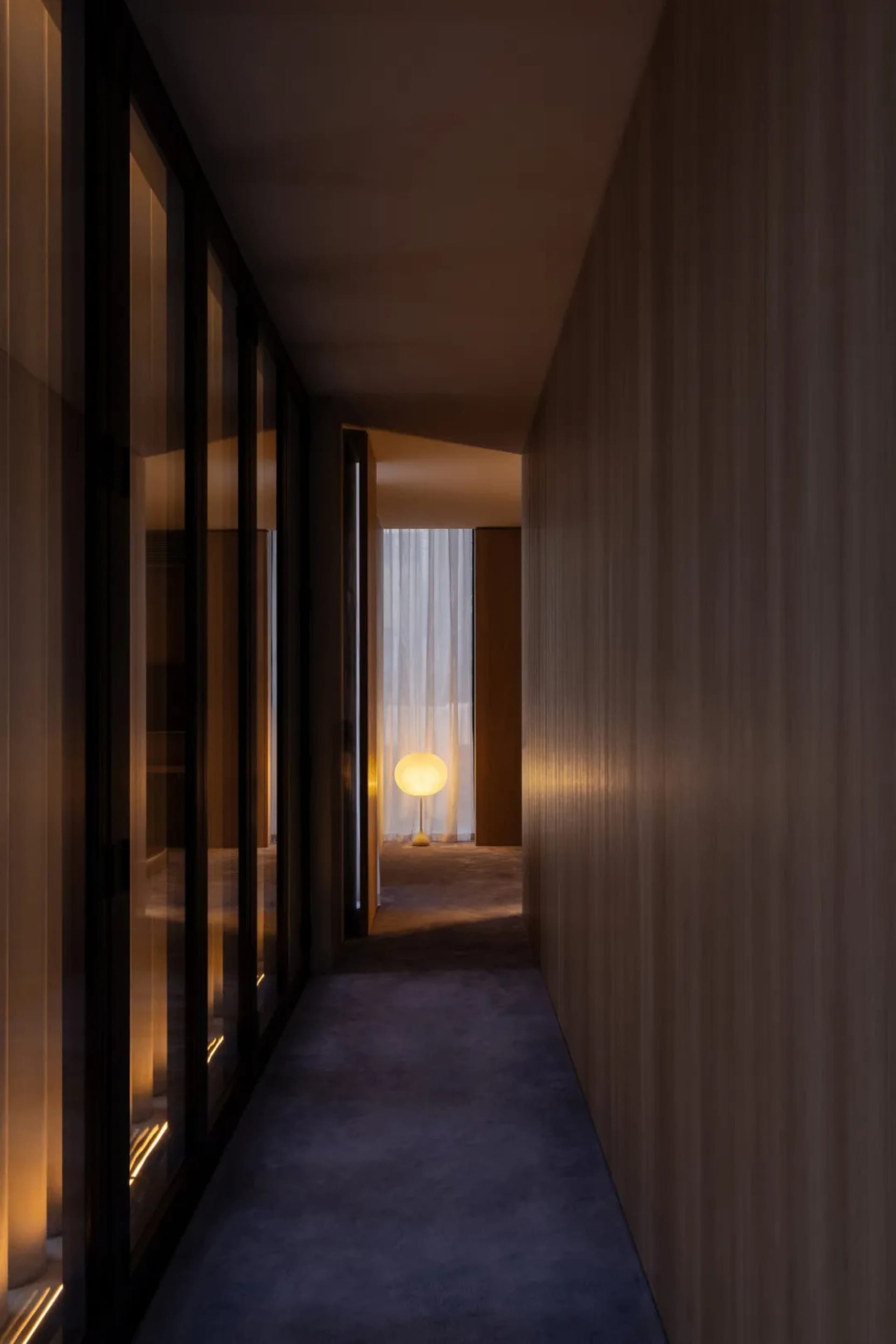 Narrow hallway with wooden floor and walls, dim lighting, and a bed on the left, creating a cozy and intimate atmosphere