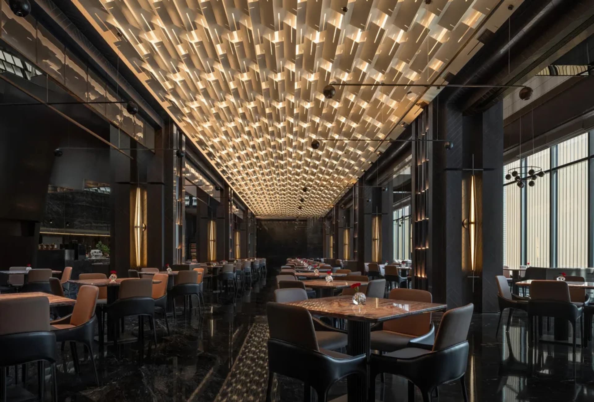 A modern restaurant with a semi-circular seating arrangement, wine glasses, and vases on tables, surrounded by a mix of black and brown colors and various materials, with soft and warm lighting