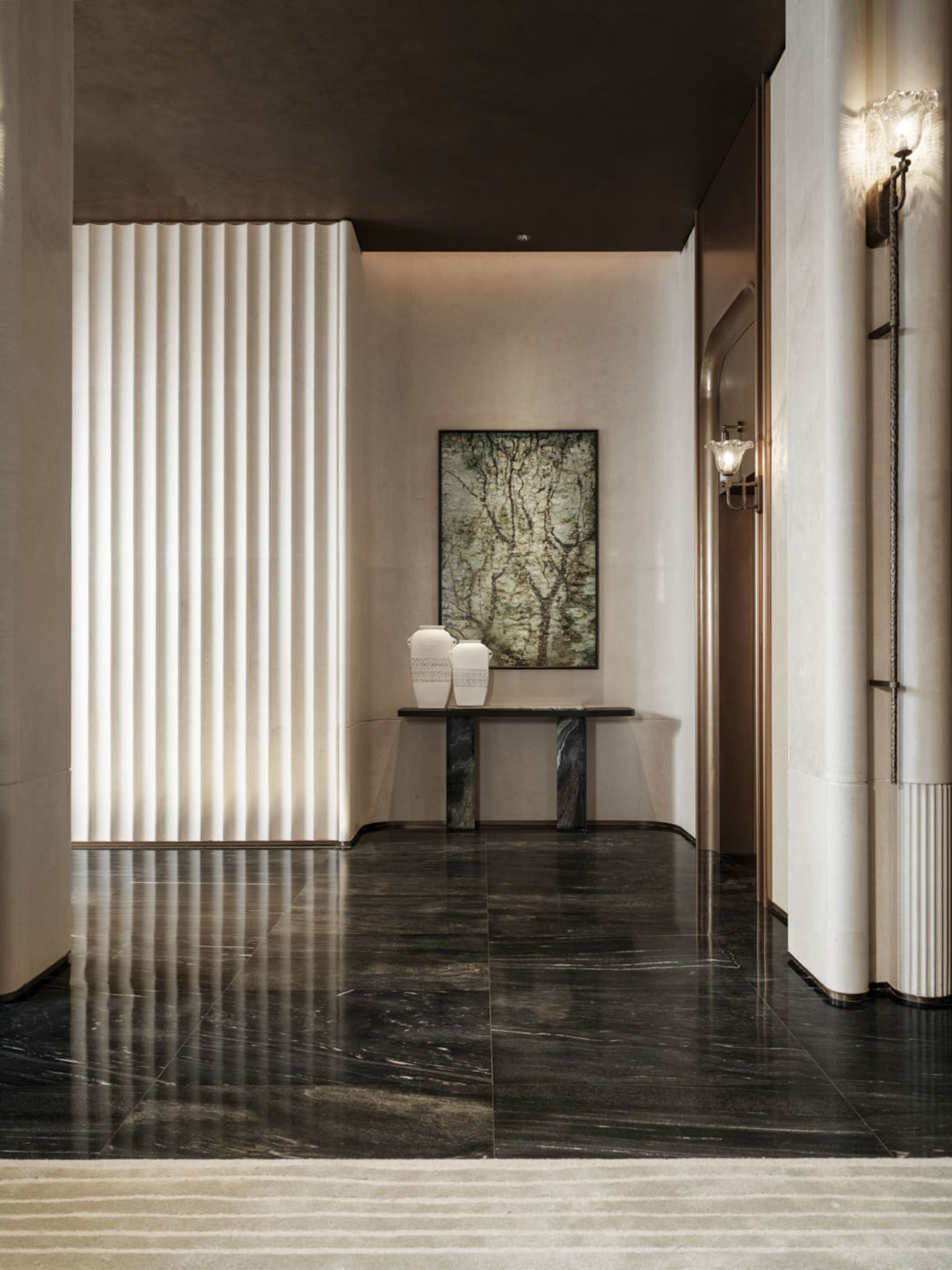 A well-lit modern hallway with a marble floor, white walls, a large painting, and decorative vases