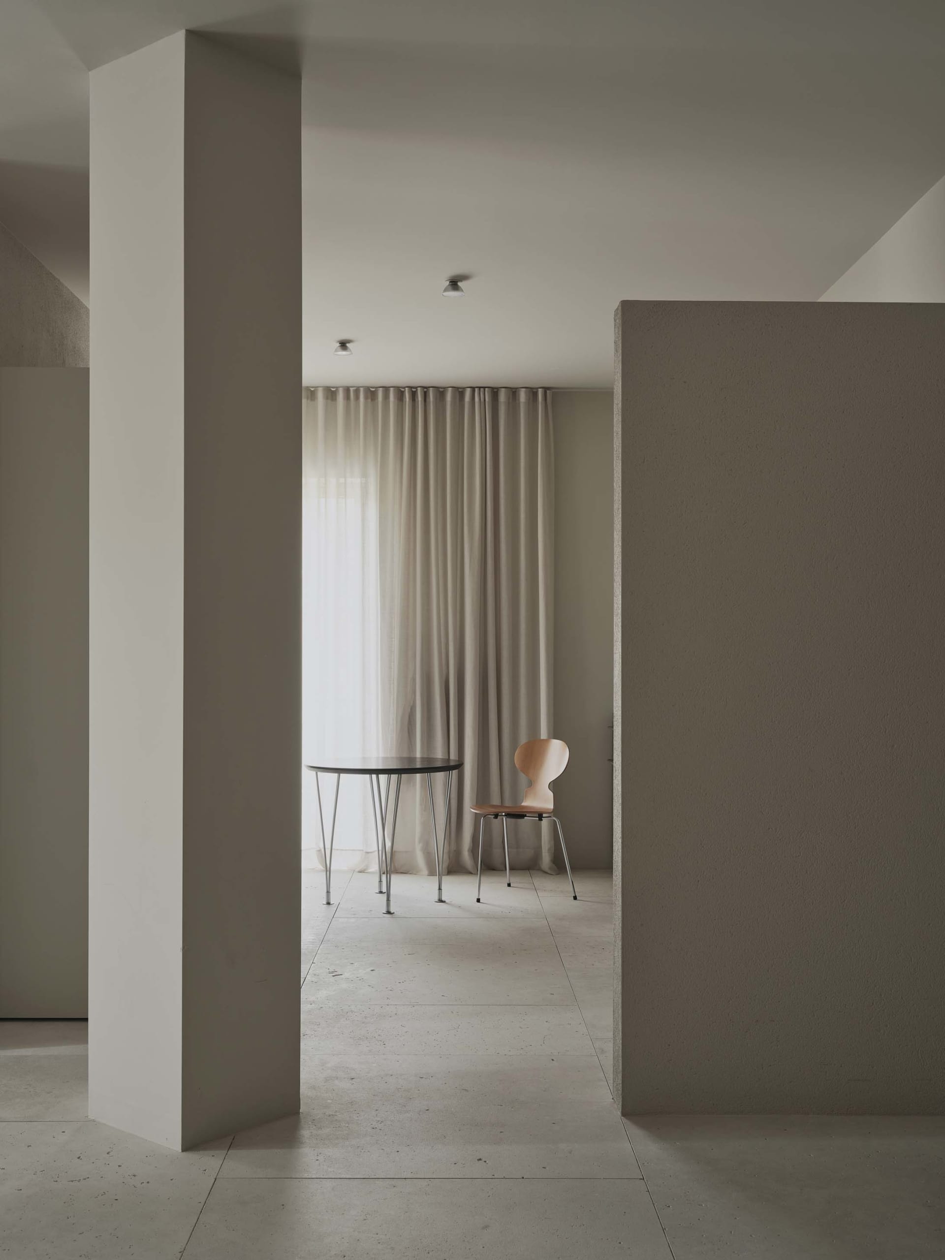 A modern dining room with a white table and chairs, surrounded by white walls and a window, with a minimalist and elegant atmosphere