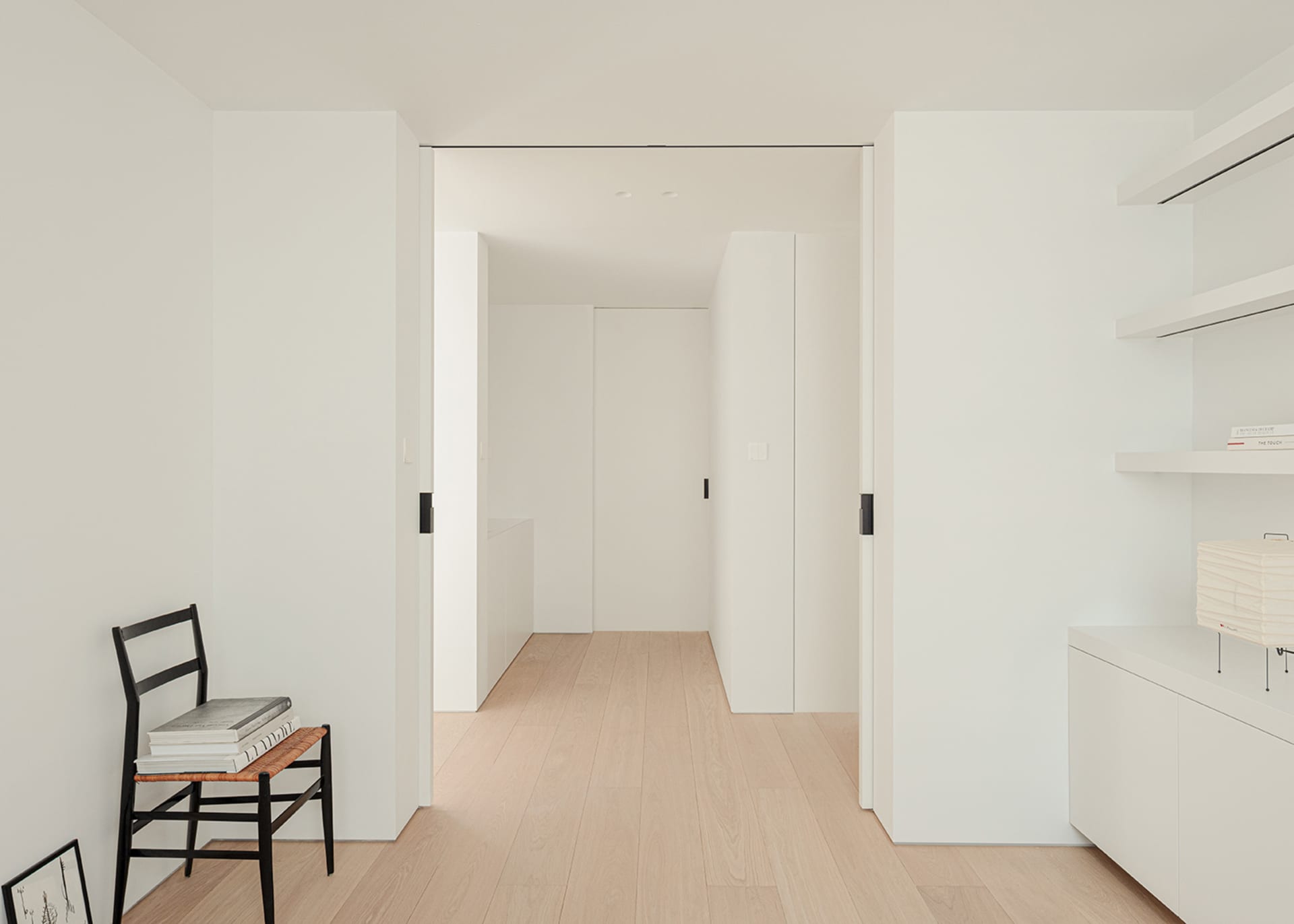 A bright and welcoming hallway with a white color scheme, wood accents, and a chair in the corner, set against a modern and clean backdrop