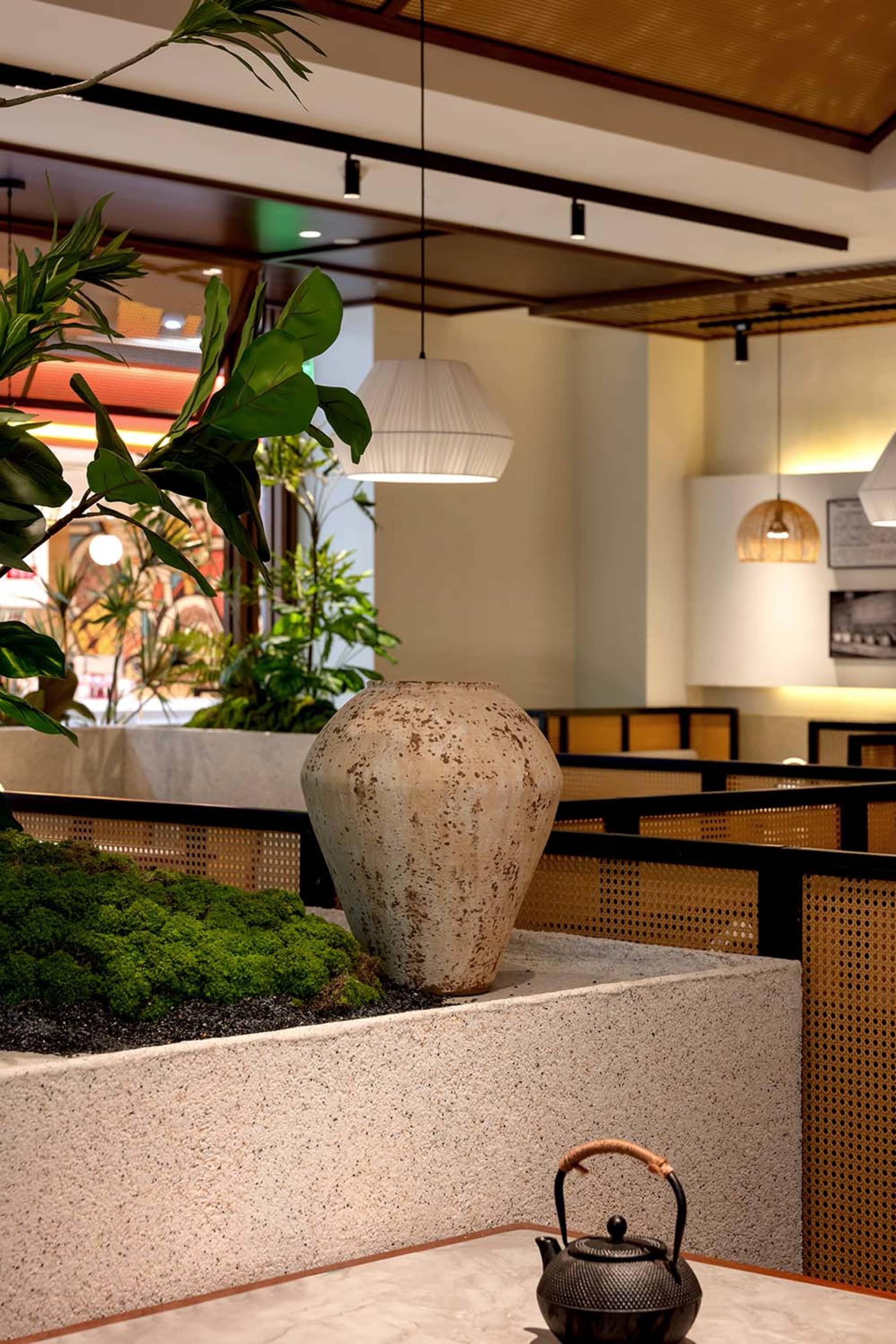 A warm and inviting restaurant interior featuring a large white vase surrounded by potted plants, adding natural beauty to the space