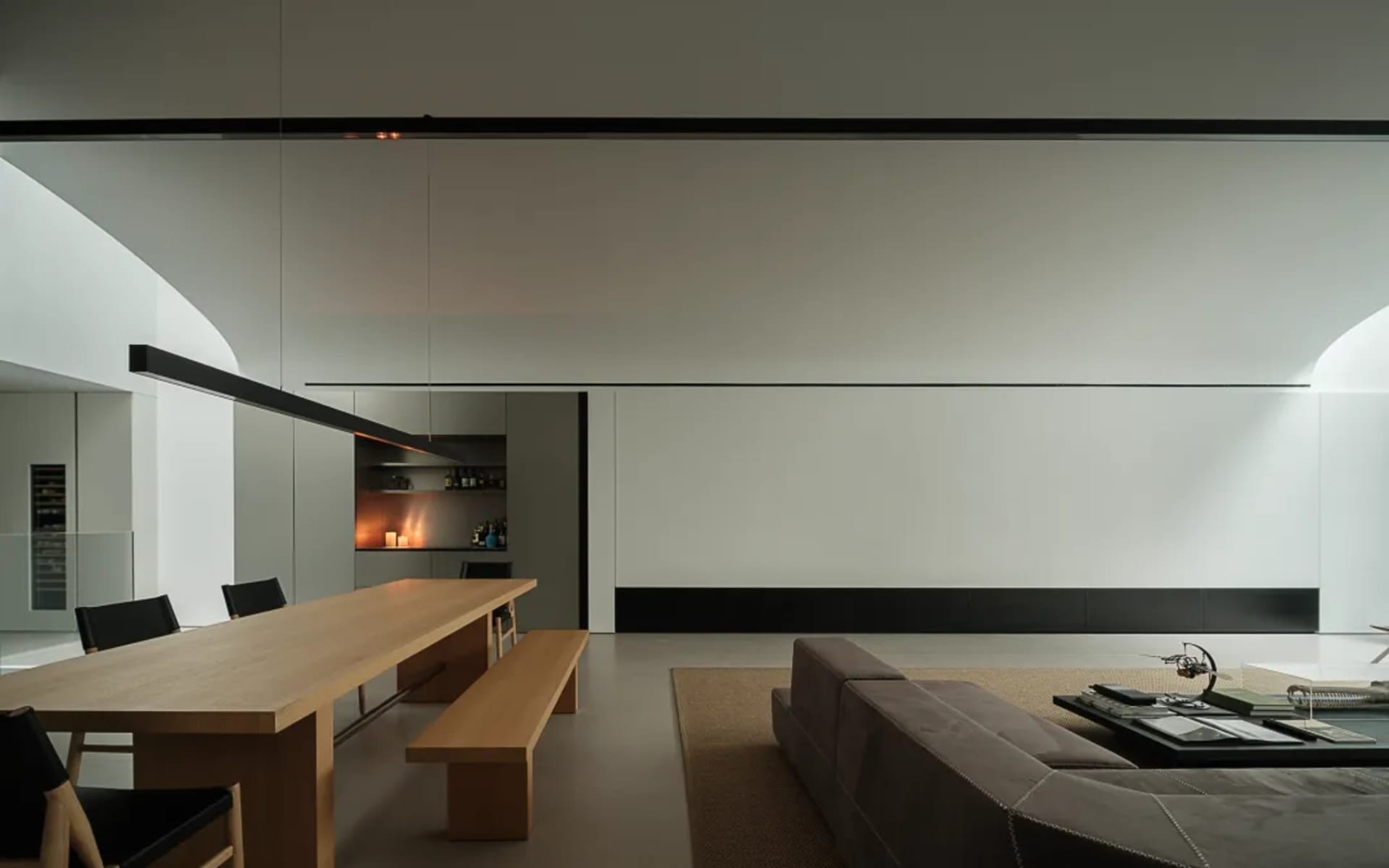 A well-lit living room and kitchen with a couch, chair, coffee table, dining table, counter, and decorative items, featuring wood and glass materials