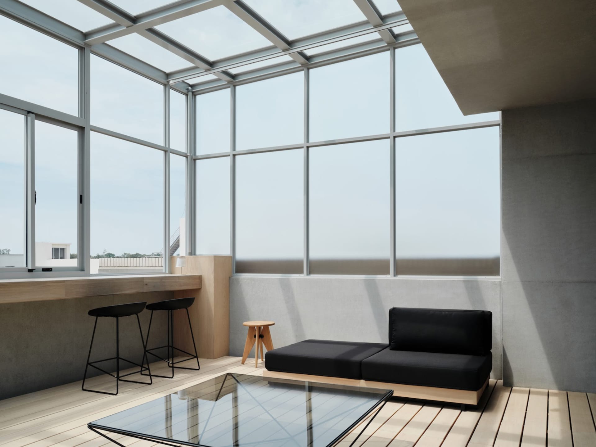 Modern living room with black and grey furniture, a glass table, and a window, lit by natural light