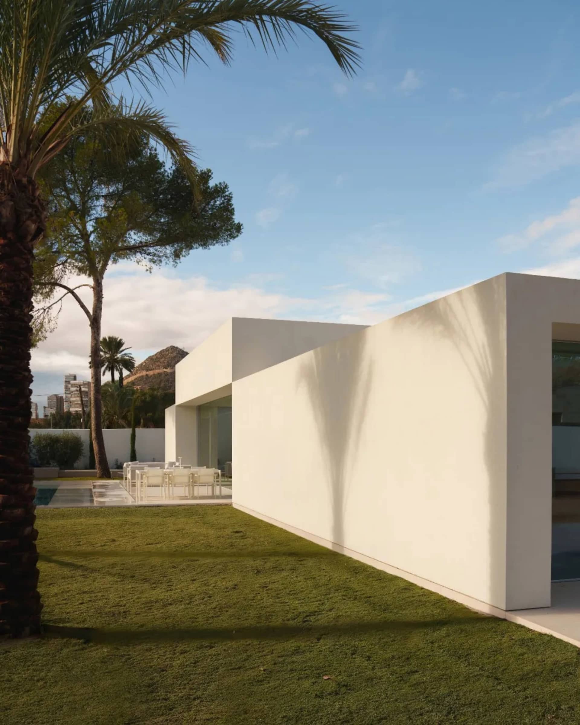 A modern house with a patio and pool surrounded by a lush green lawn, well-lit with natural light
