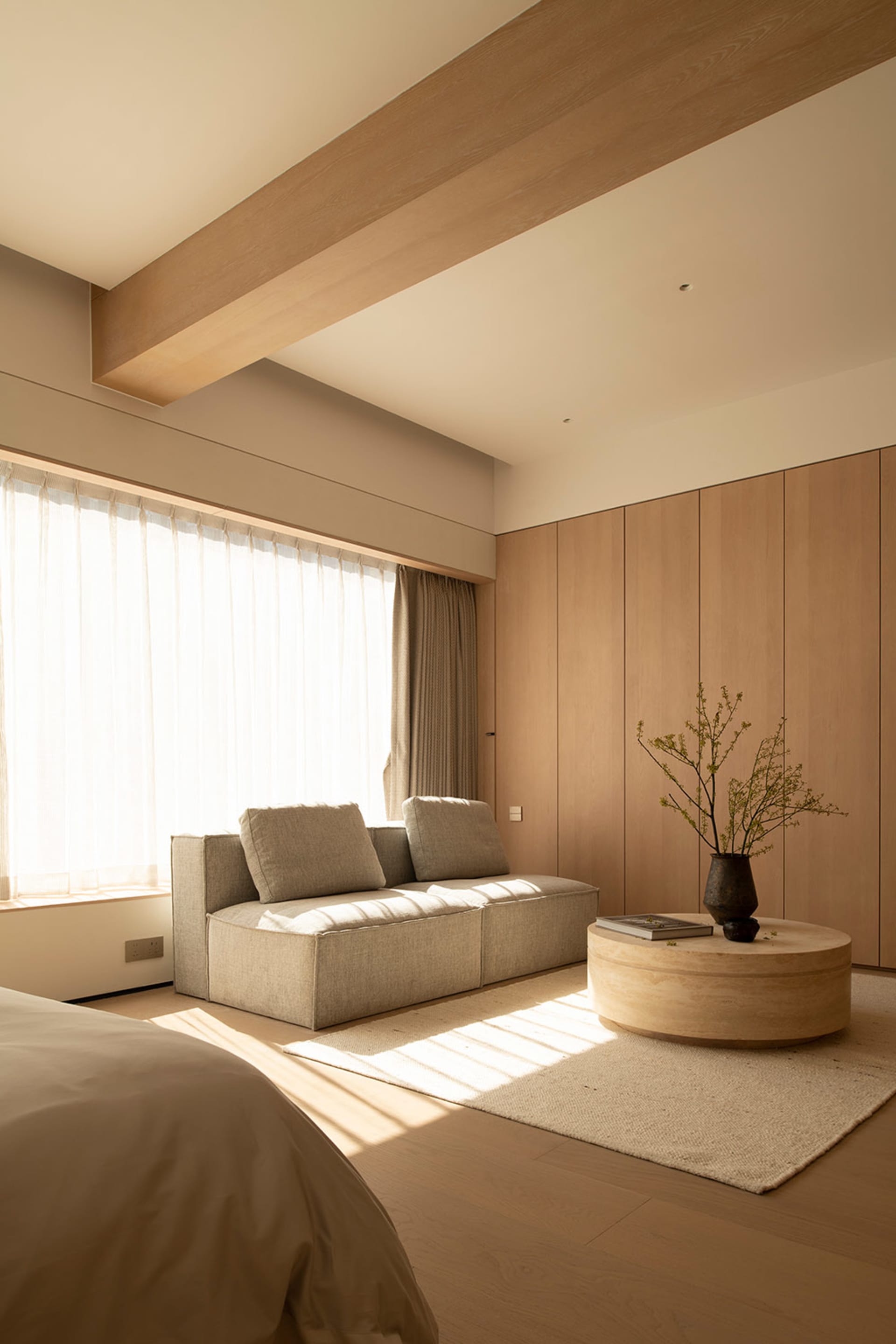 A modern living room with a gray couch, a wooden chair, and a coffee table, lit by natural light from a large window