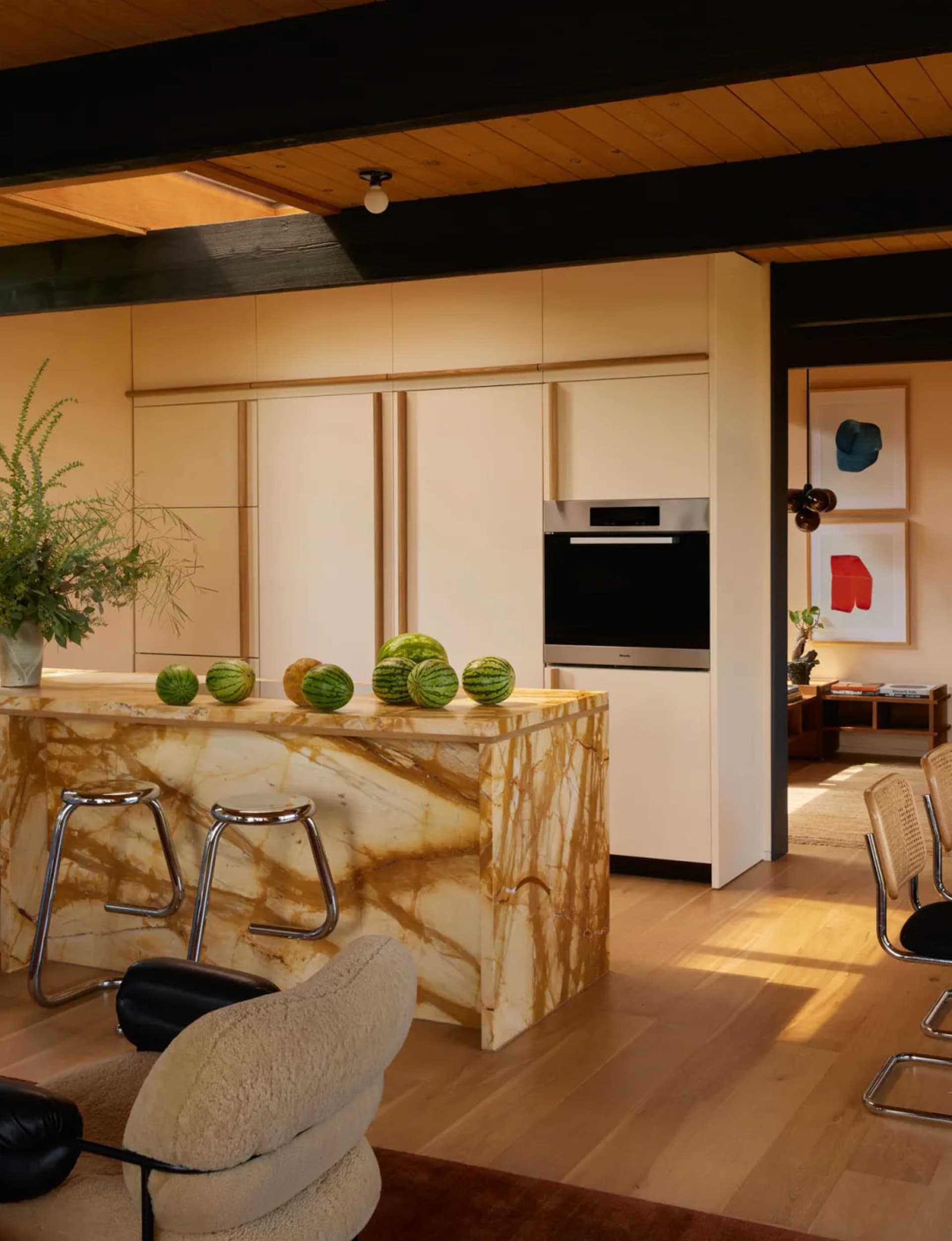 Modern kitchen with a marble countertop, featuring a refrigerator, oven, and sink, with natural light and comfortable seating