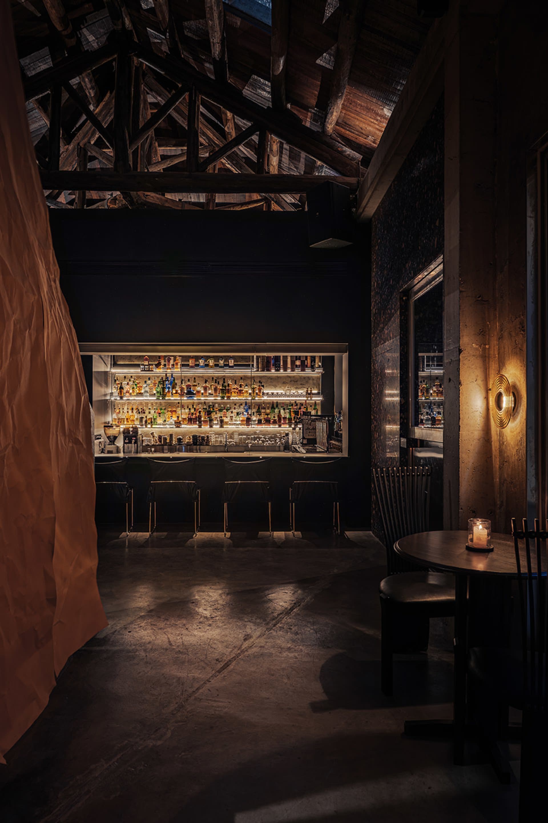 A dimly lit bar with a black and white color scheme, featuring a display of liquor bottles, chairs, and a dining table