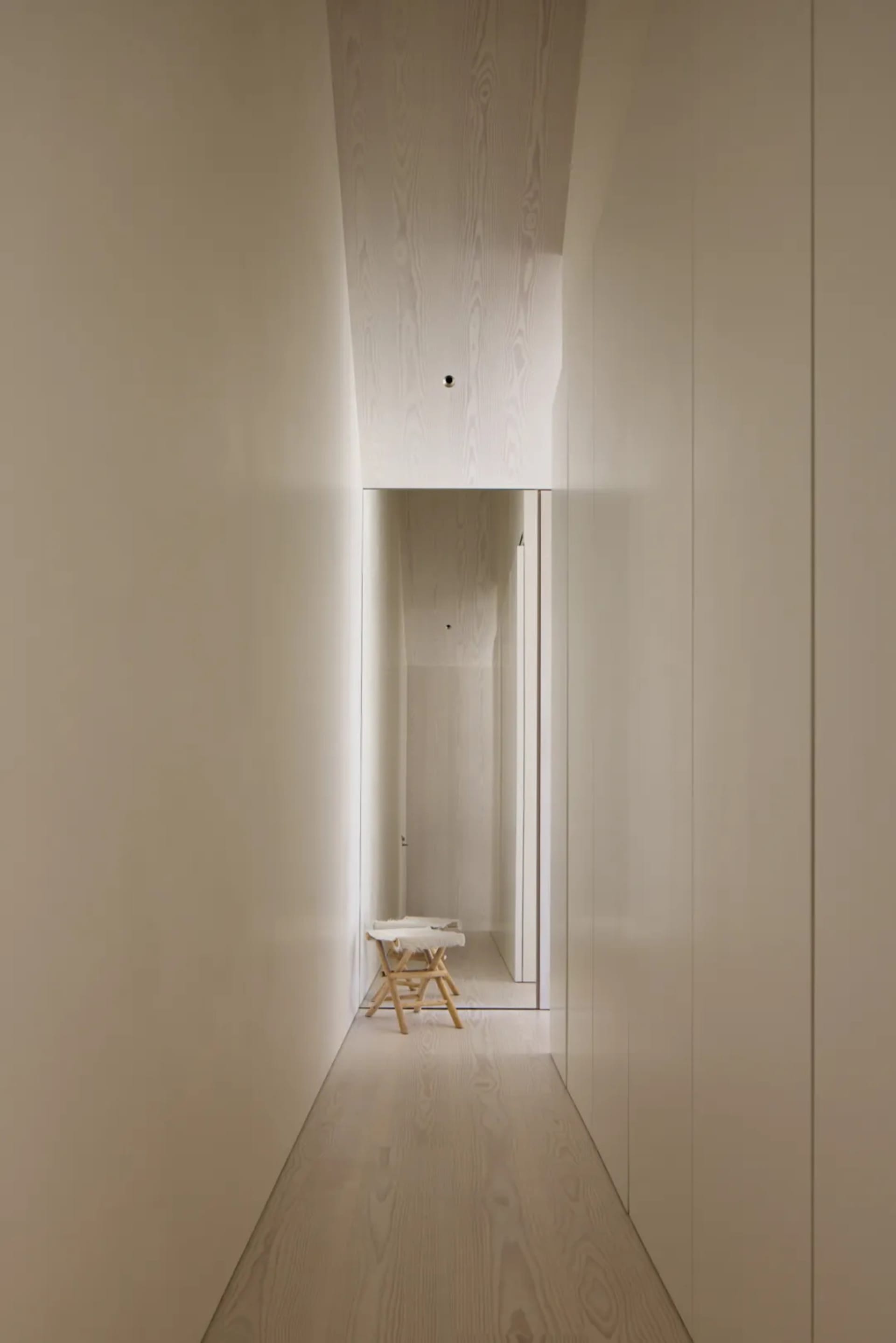 Narrow hallway with a white color scheme, a small table, and a chair, creating a cozy atmosphere with dim lighting