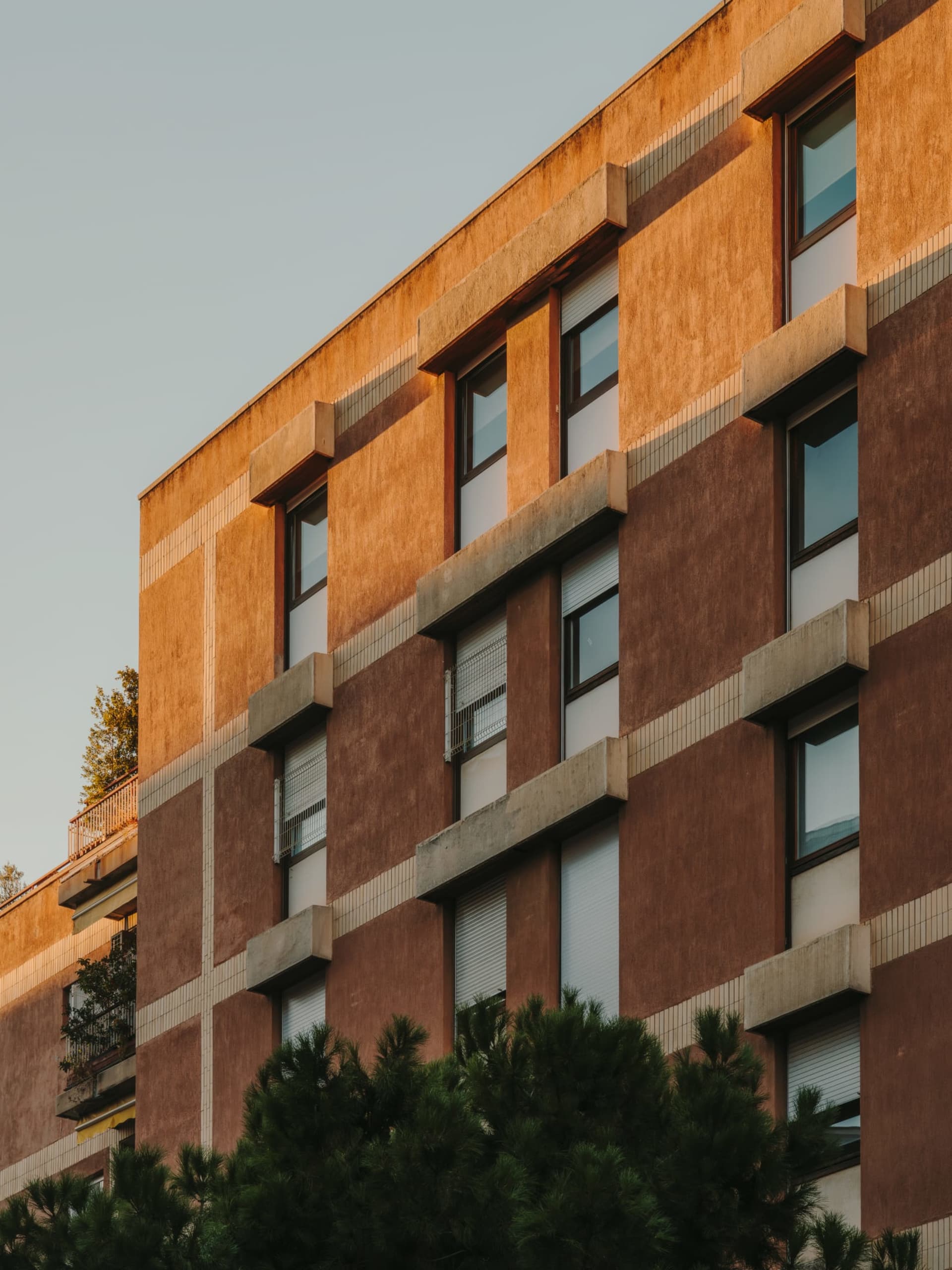 Photograph of a modern building with a brick facade, featuring a mix of brown and white colors, and numerous glass windows
