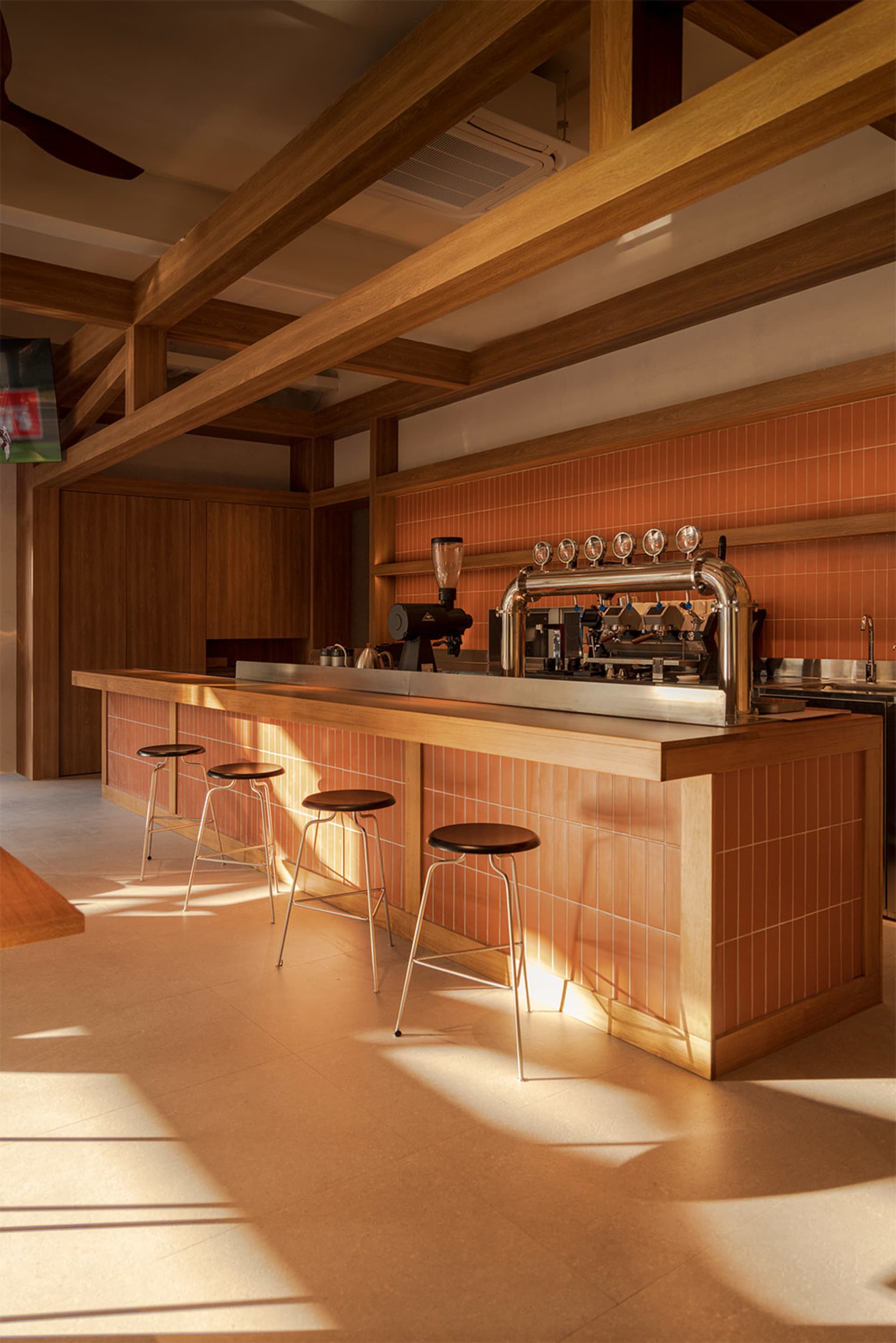 A well-lit bar area with a wooden counter, black stools, and a coffee machine in a restaurant setting, featuring natural lighting and high-quality materials