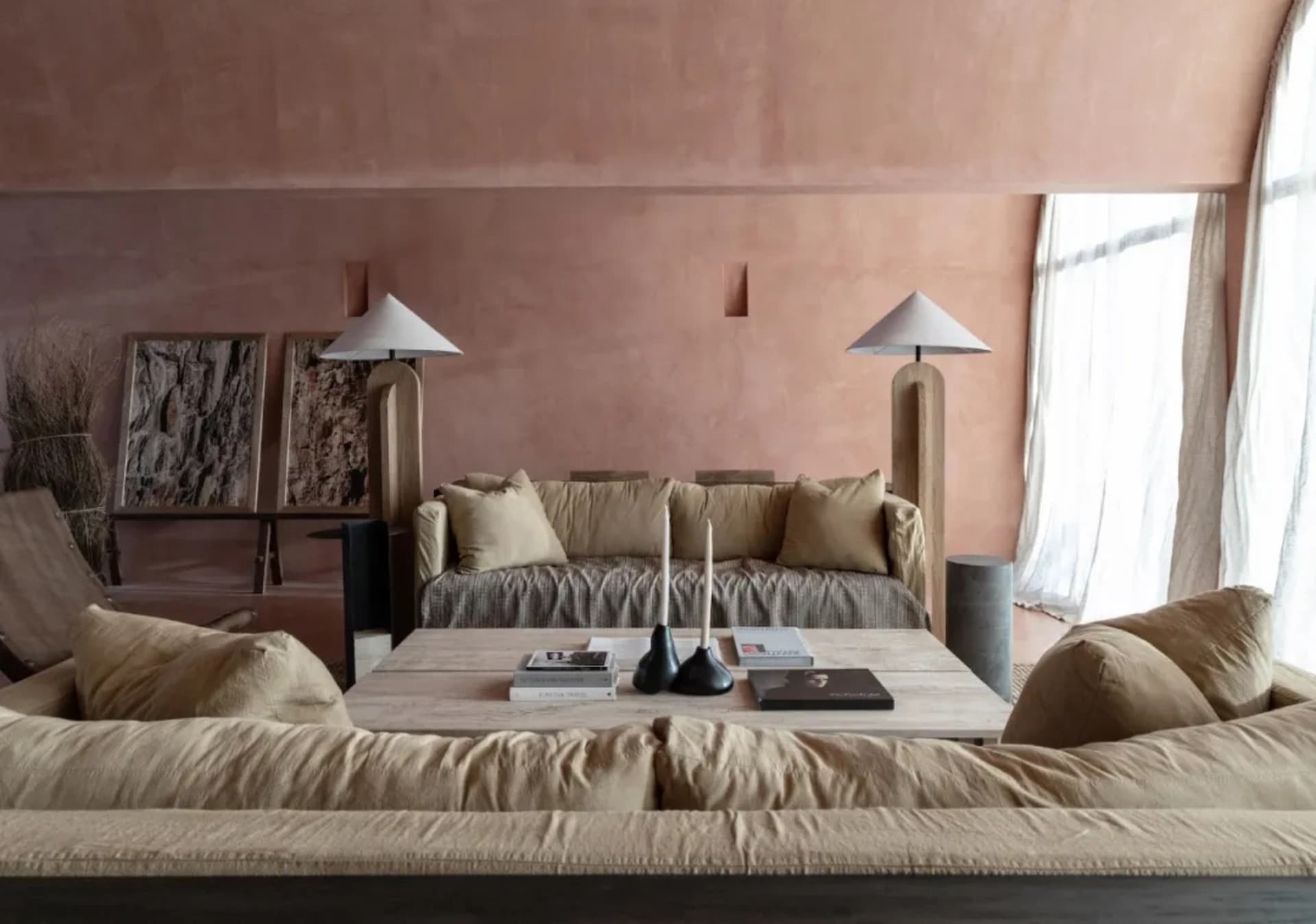 Cozy modern living room with a pink wall, brown couch, and dining table surrounded by chairs, with a bookshelf and two lamps