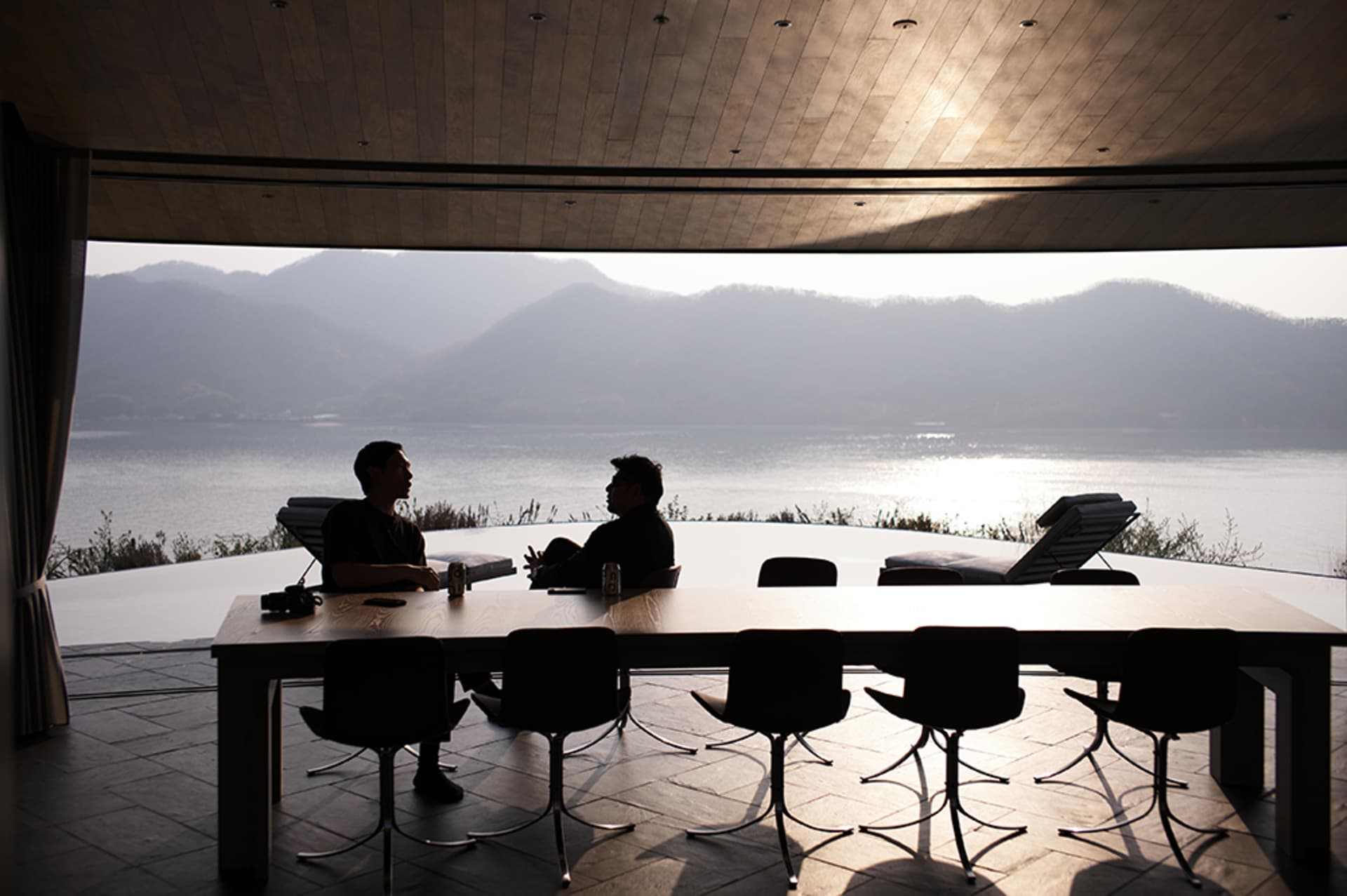 A cozy dining room with a large wooden table and black chairs, surrounded by a view of the water