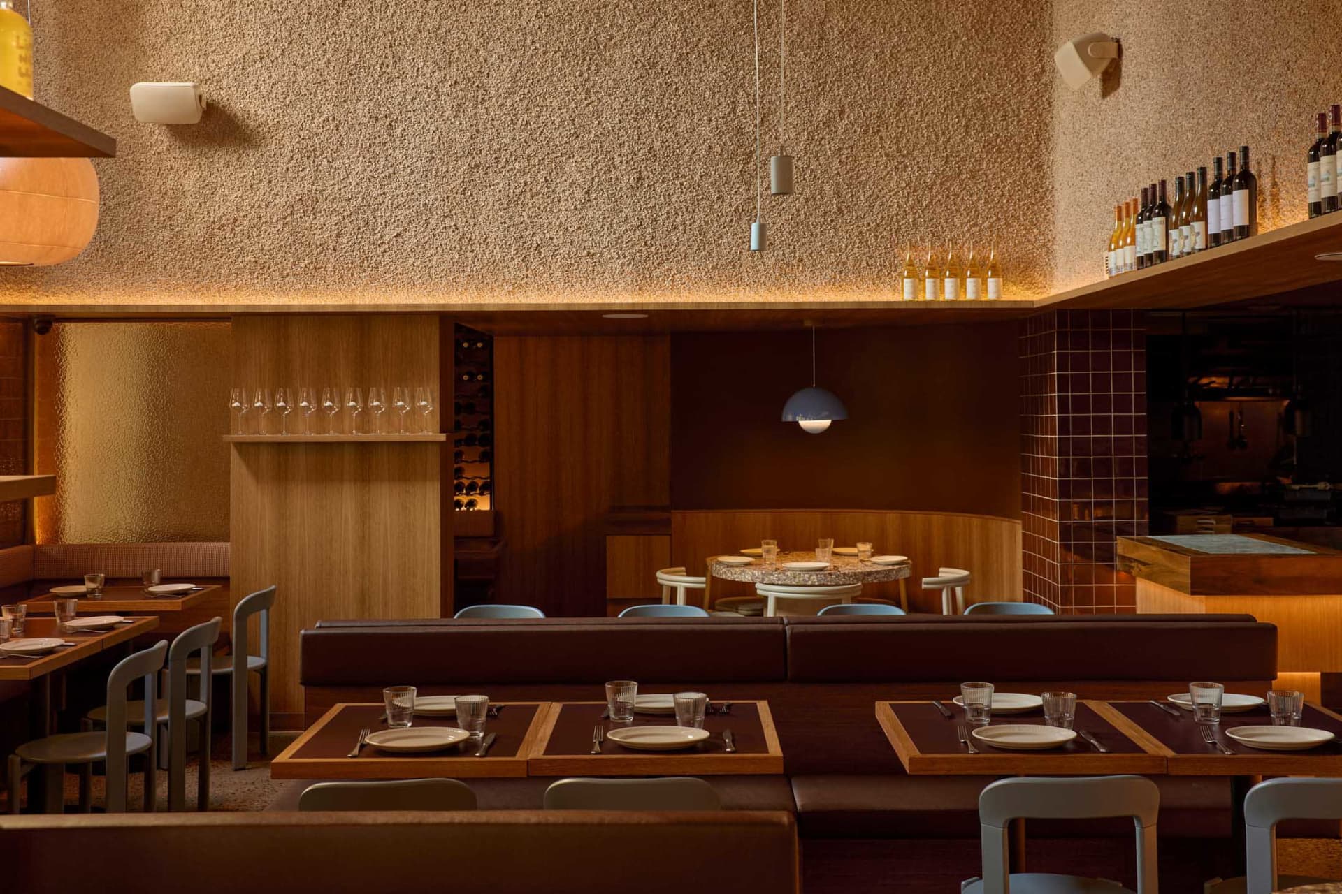 A well-lit restaurant dining area with a long wooden table and comfortable chairs, surrounded by wine glasses, cups, and bowls