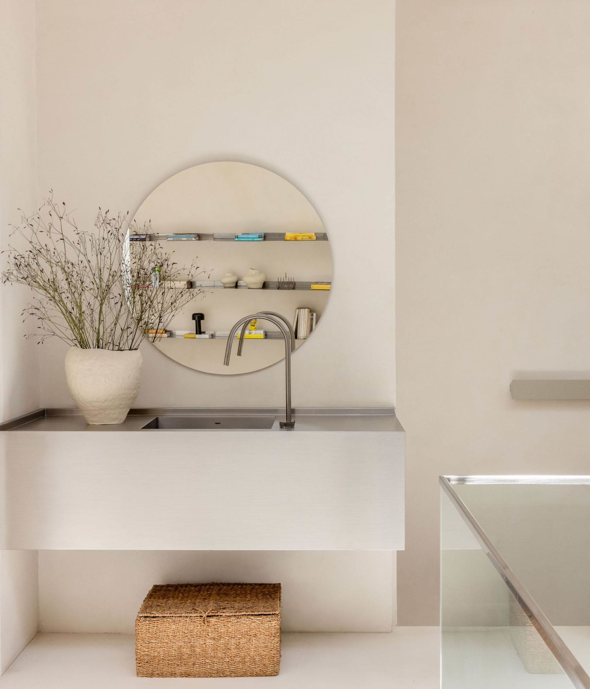 A well-lit bathroom with a sink, mirror, and vase, featuring predominantly white materials