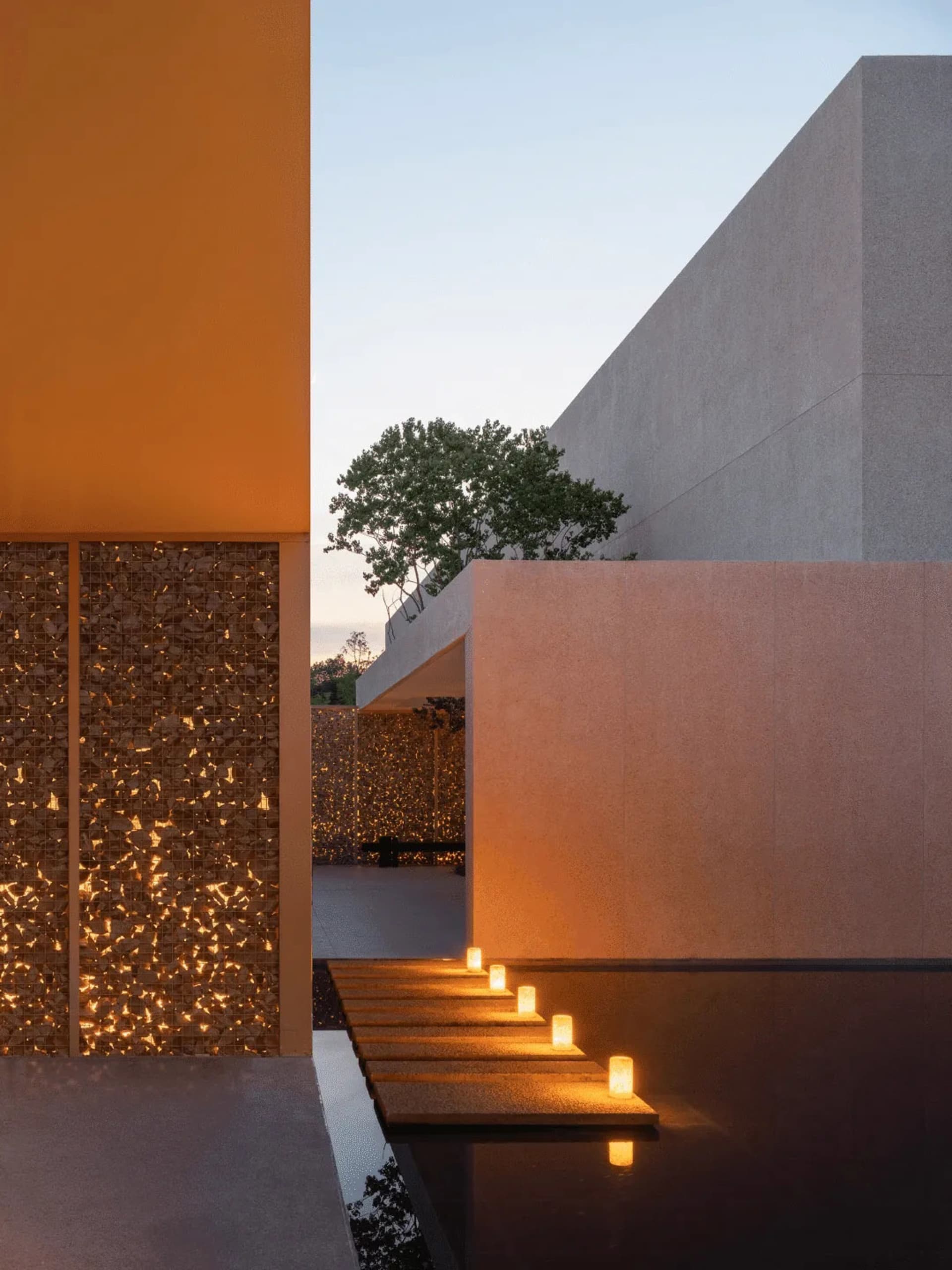 Photograph of a modern building with a glass wall, stone exterior, and warm candlelight interior