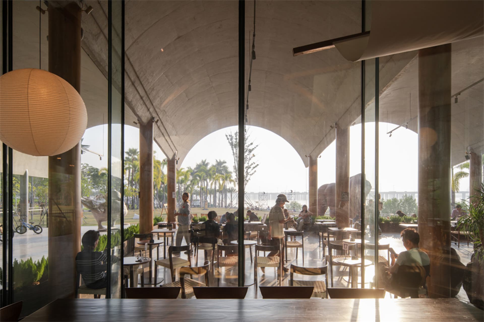A modern restaurant with a glass wall, wood furniture, and natural light, located near a body of water