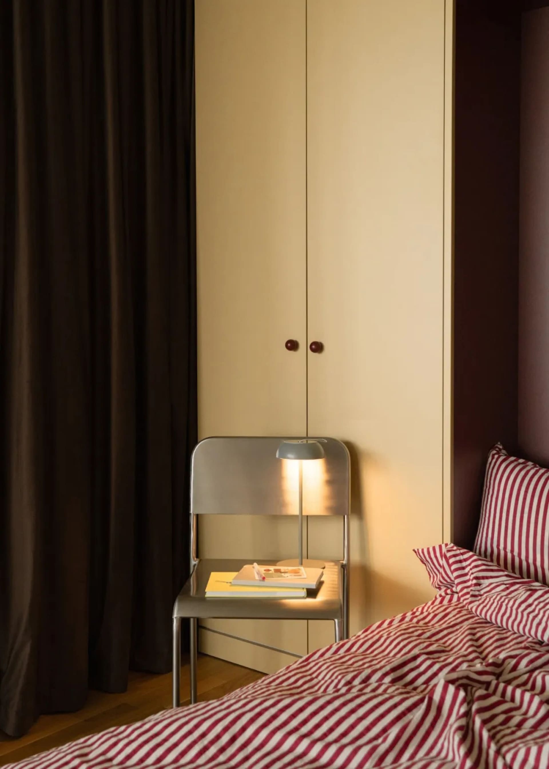 Cozy bedroom with a bed, chair, and dresser, dimly lit with red walls and wooden furniture