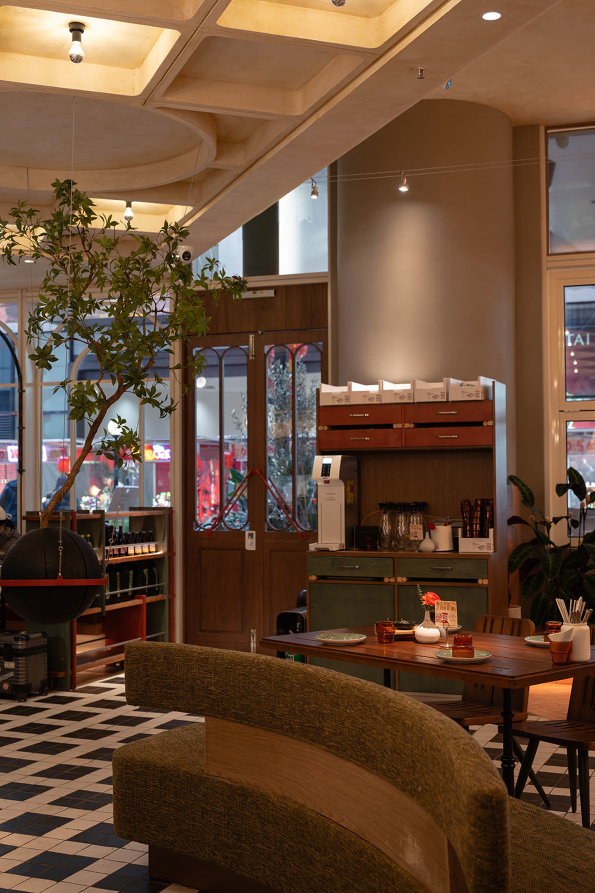 A cozy cafe interior with a wooden table and chairs, surrounded by decorative items and a potted plant, under soft warm lighting