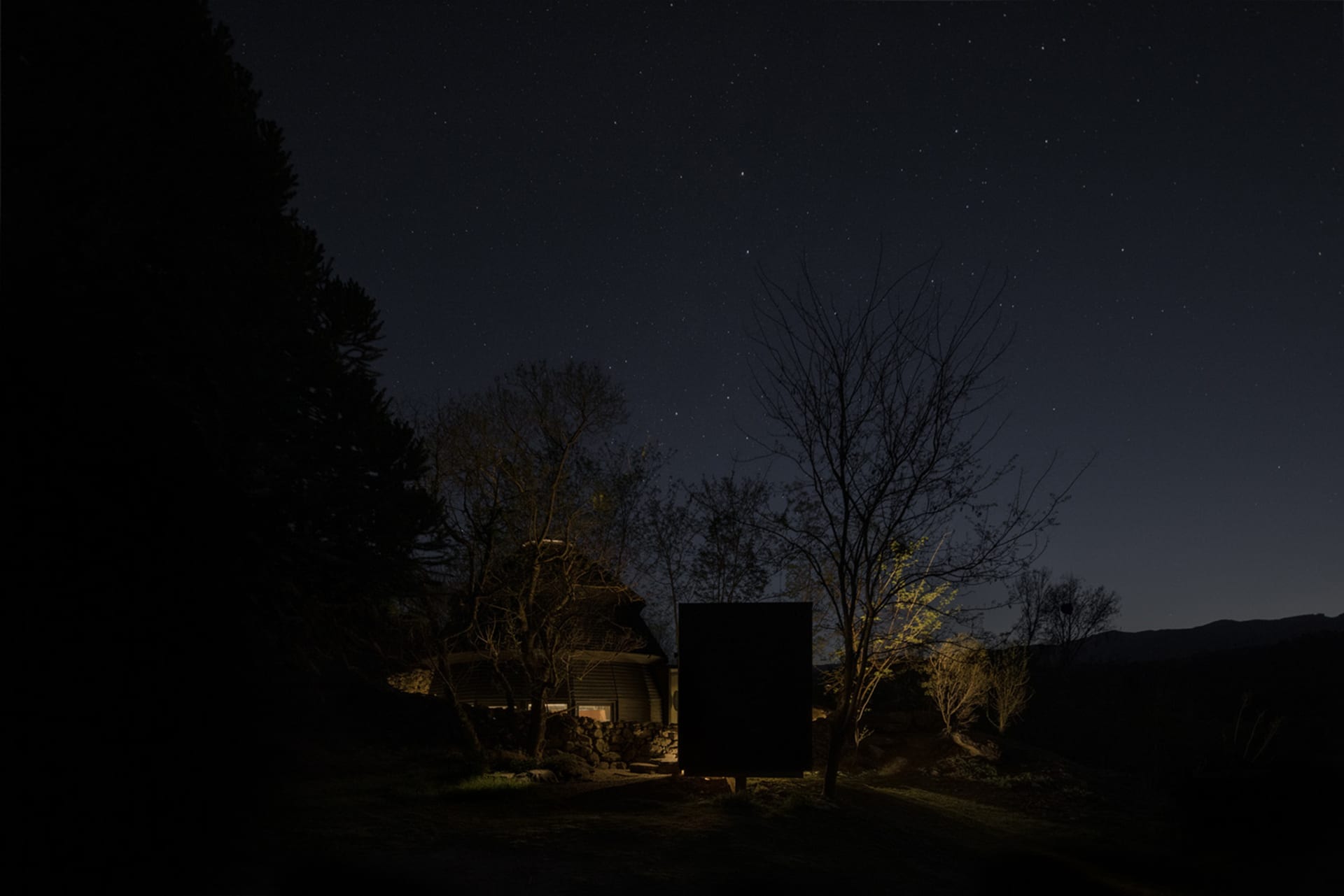 A house surrounded by trees, featuring a black shed in the yard, blending into the natural environment