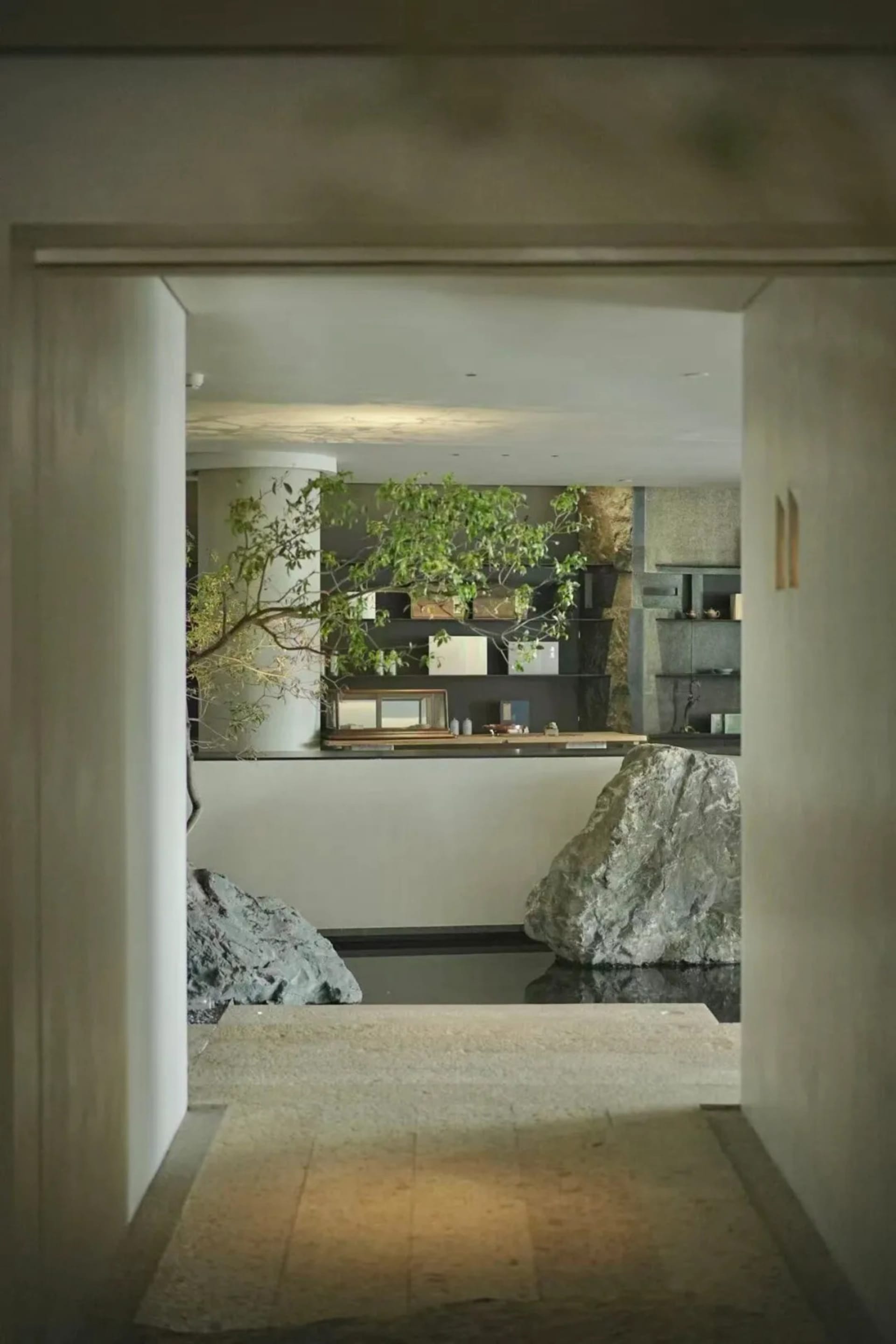 Cozy dining space with a rock wall, a large rock, and a modern dining table and chairs, decorated with a potted plant and vases, in a dimly lit room