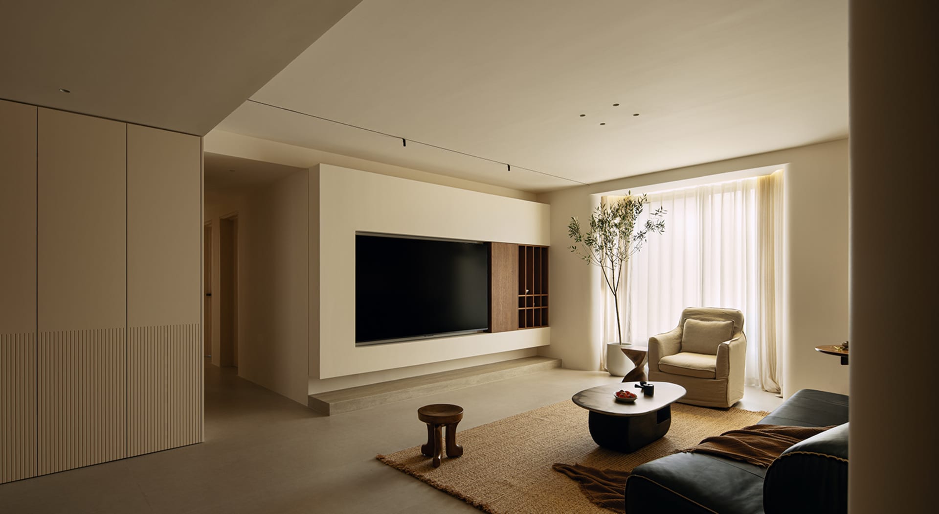 Cozy modern living space with a flat screen TV, a couch, a chair, a coffee table, and a potted plant, lit by natural and artificial light