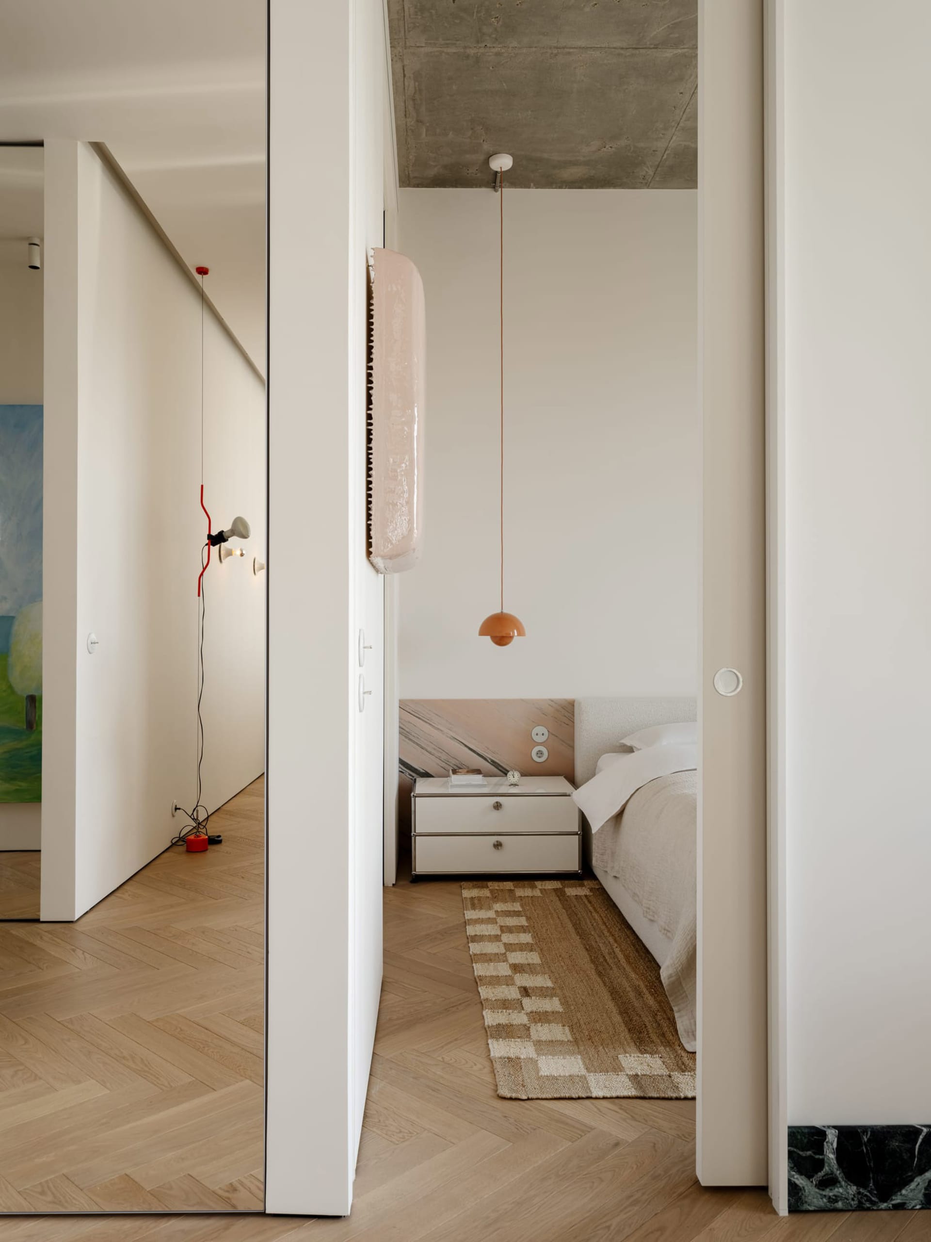 A small white bedroom with a bed positioned under a mirror, a dresser, and a calm atmosphere