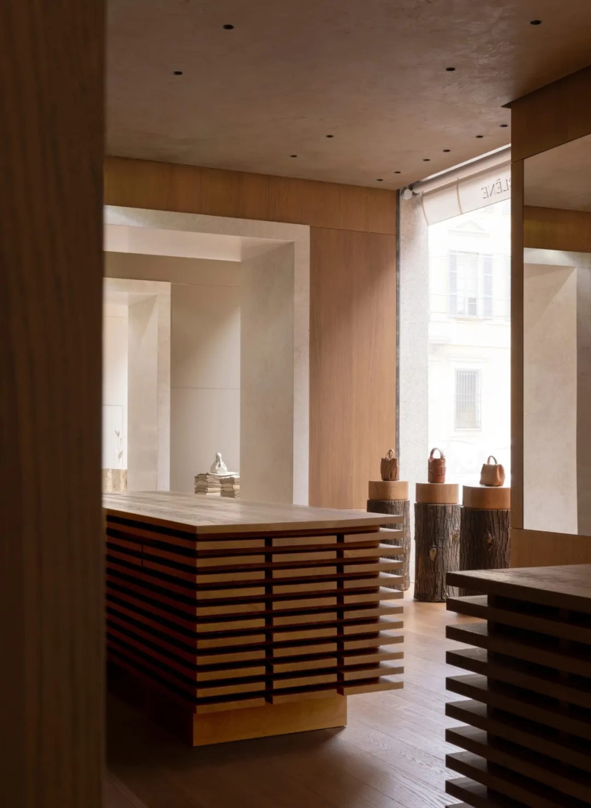 A modern kitchen and dining area with a wooden floor, a large window, a dining table, and a counter, decorated with vases and featuring a clean, minimalist design with natural materials