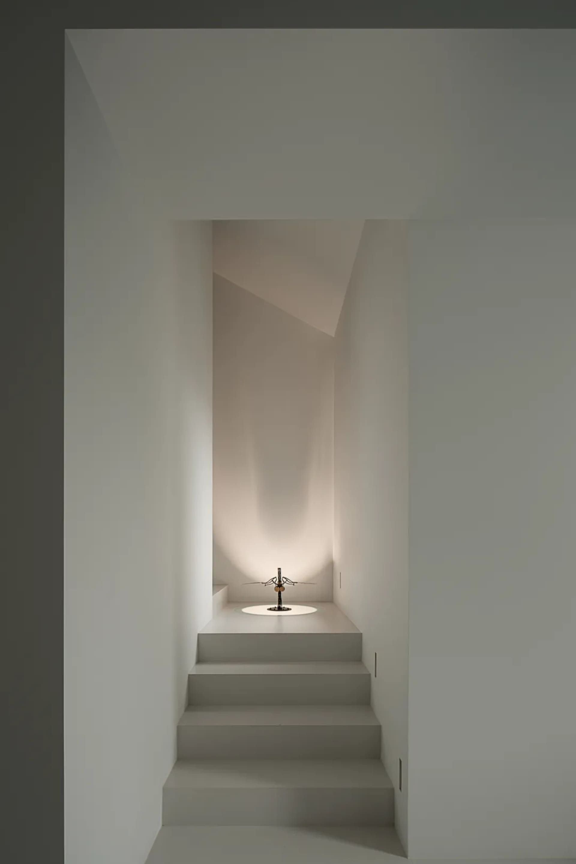A dimly lit narrow hallway with a staircase made of concrete and a light in the corner, casting a warm glow