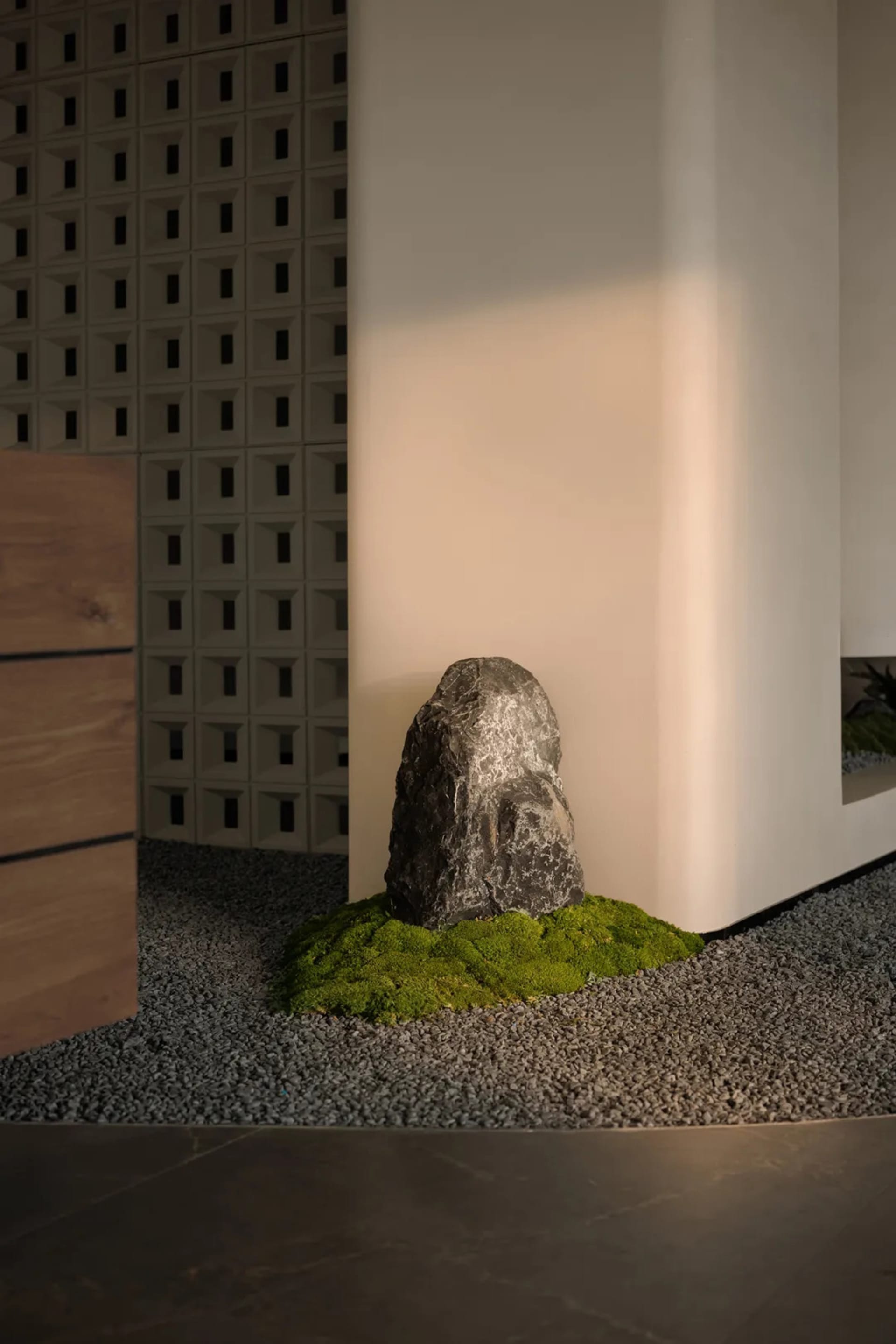 A serene room with a rock on a bed of moss, surrounded by a white wall and a wooden cabinet, on a gravel surface