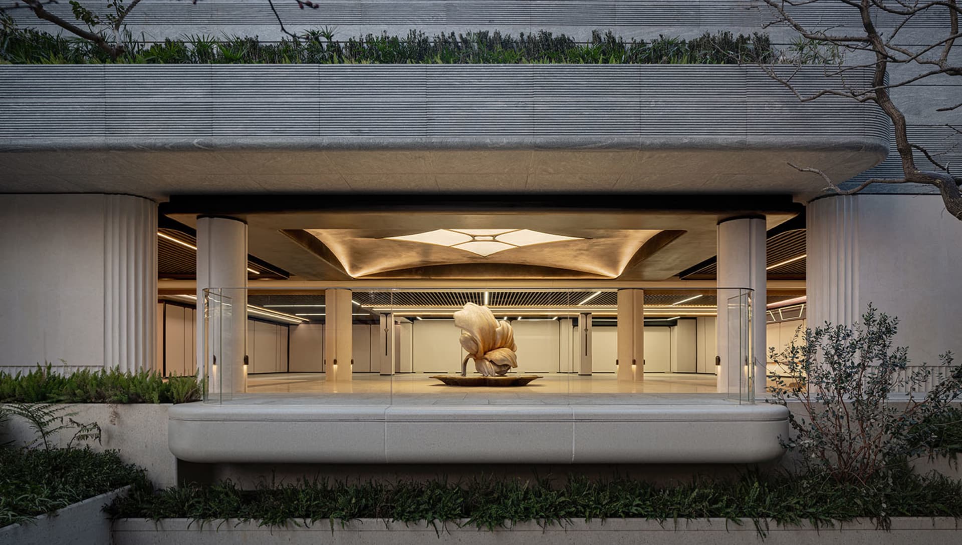 A dimly lit, modern building lobby with a large metal sculpture as the centerpiece, surrounded by concrete walls and floors