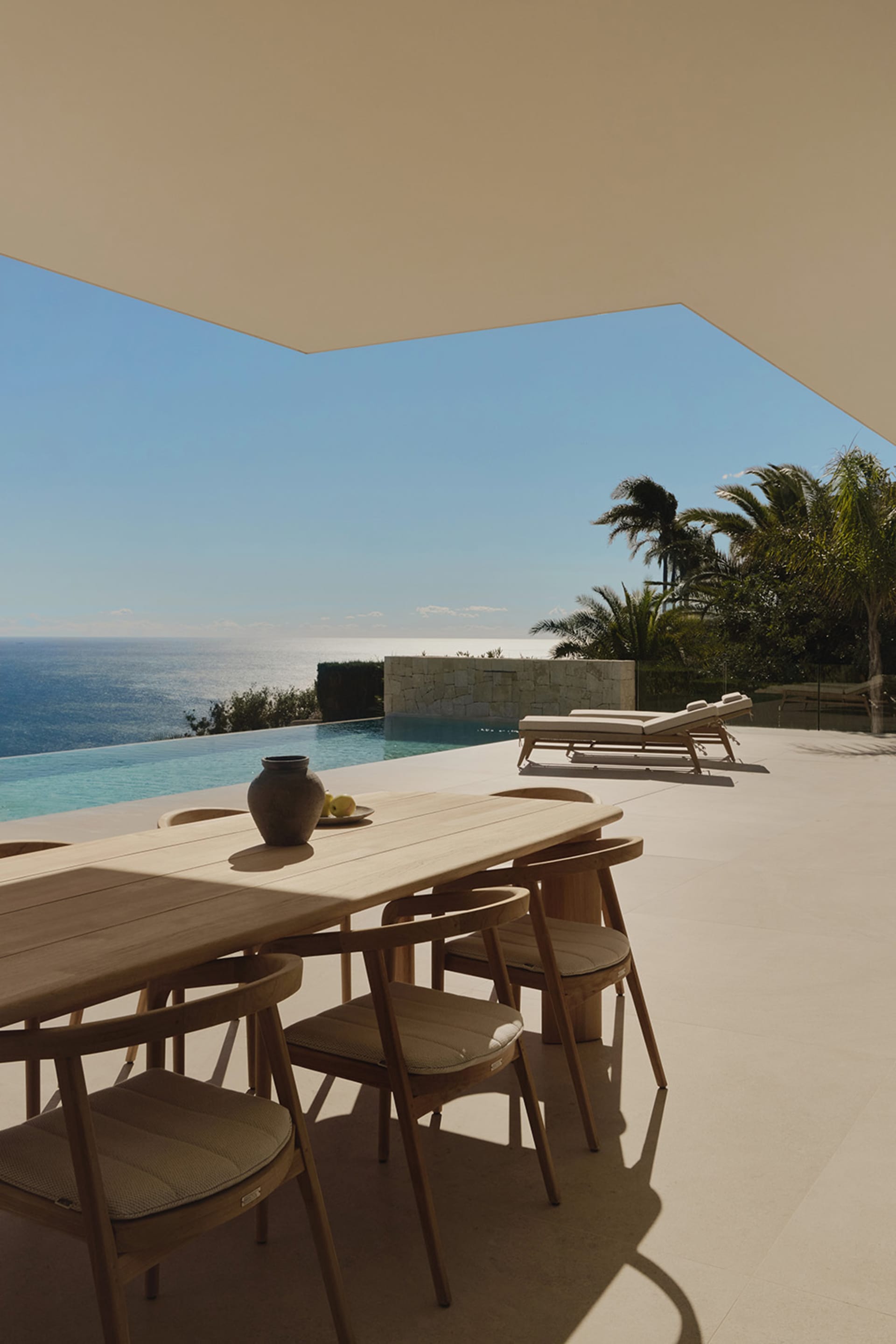 A modern outdoor living space with a wooden dining table, lounge chair, and couch, surrounded by chairs and a bench, set in a well-lit patio area with a harmonious color palette