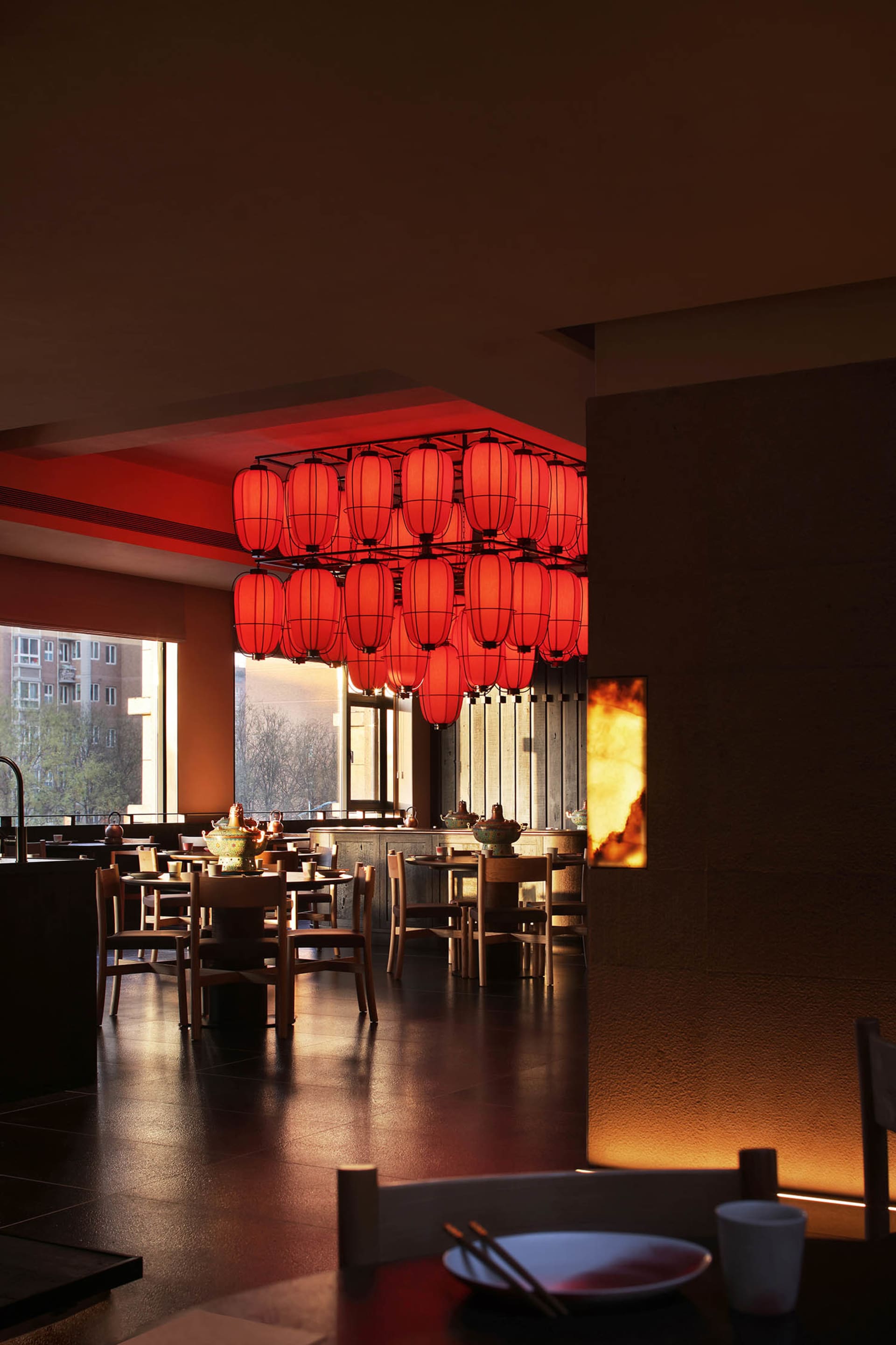 A warm and inviting restaurant dining area with a large red and white chandelier, multiple chairs and tables, and natural light from the windows