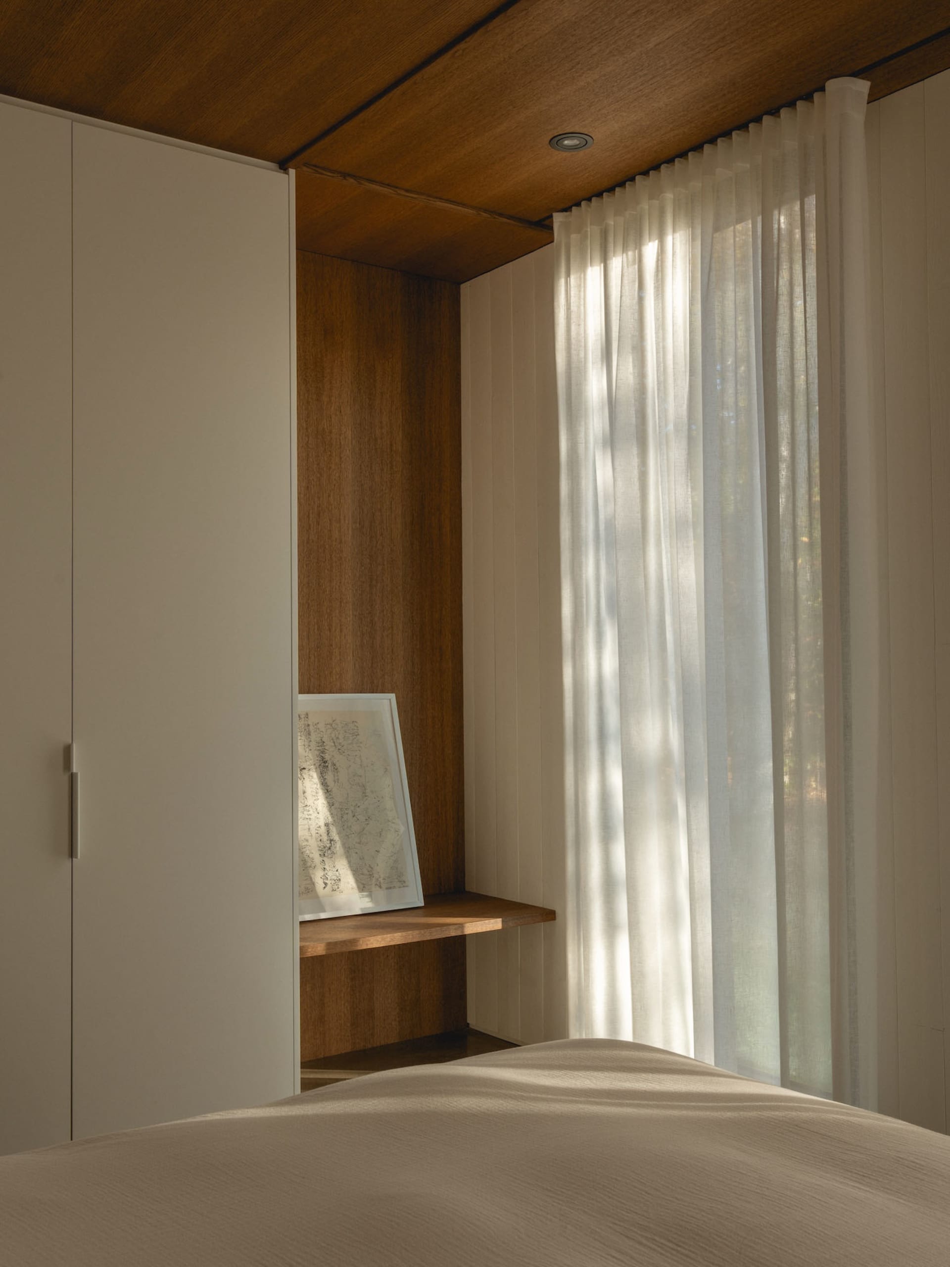 A calm and inviting bedroom with a white bed, a wooden dresser, and natural light from a window