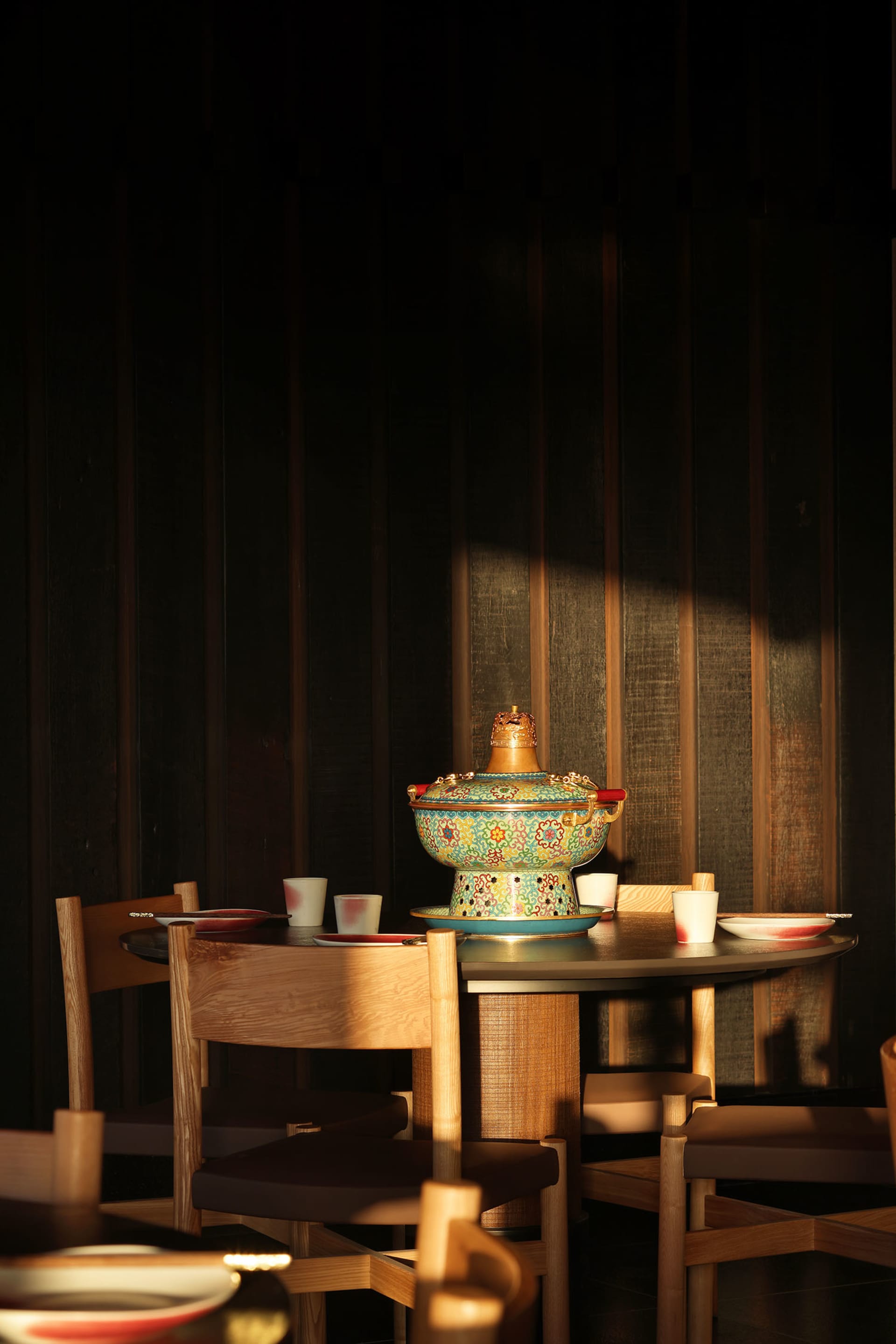 Dining room with a wooden table and chairs, surrounded by a wooden floor and a wall, with a vase on the table and various dishes set out