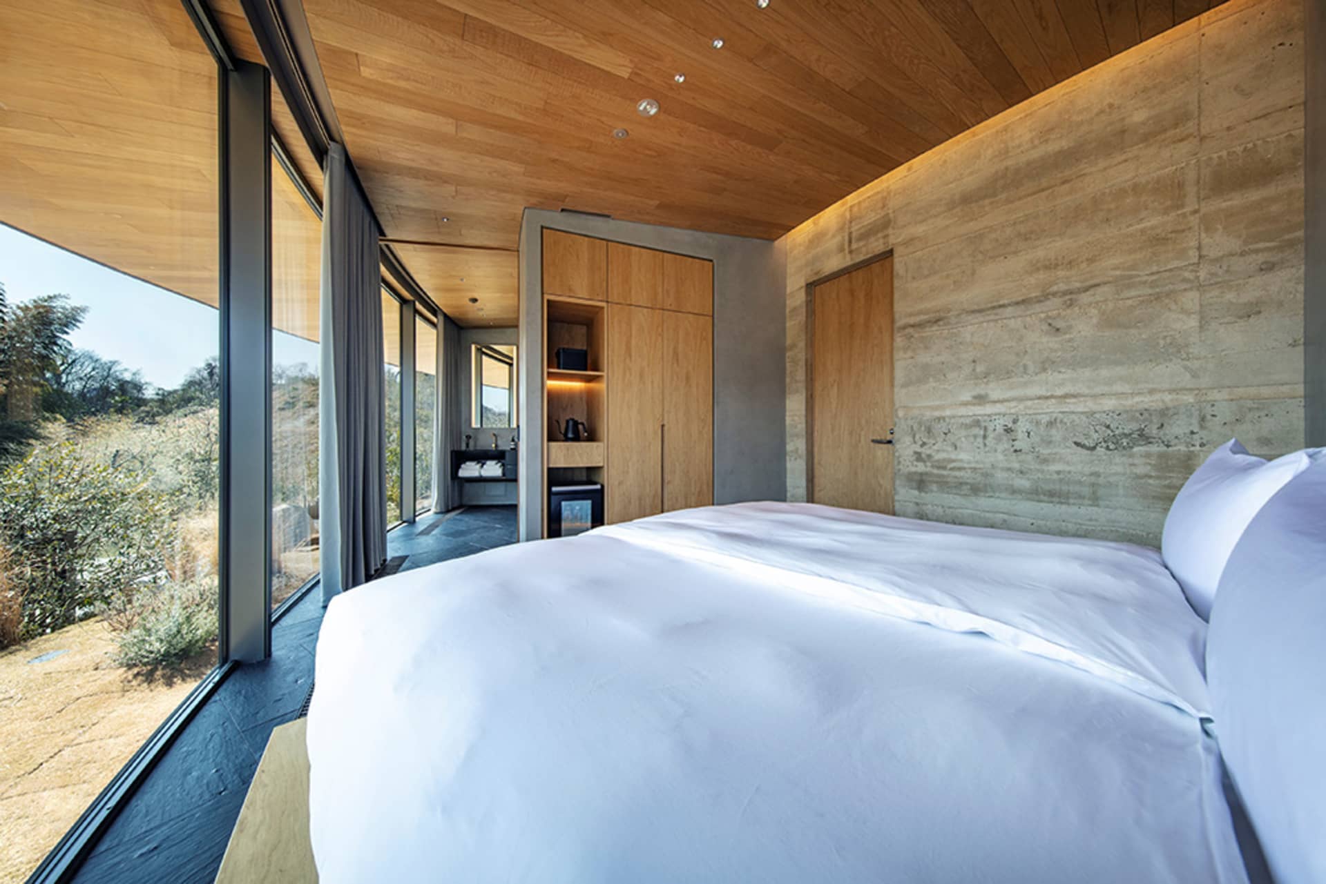 Cozy modern bedroom with a wooden floor, a large bed, a desk, and a chair, with natural light from a window